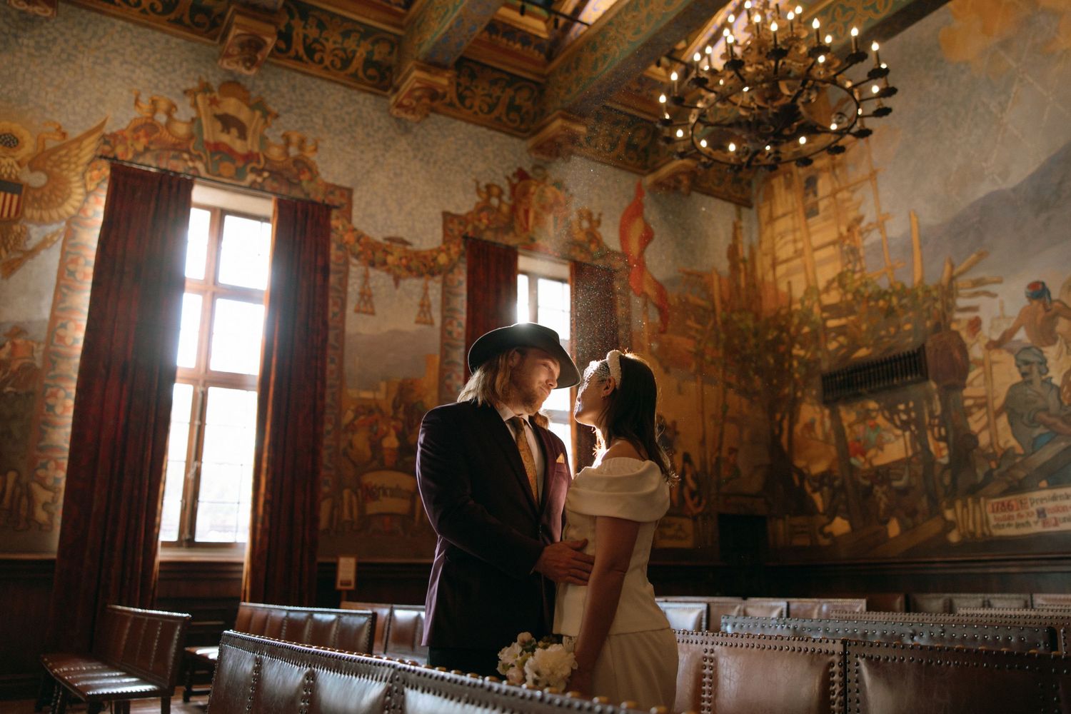 Bride and groom sharing an intimate moment in an ornate room with historic painted murals.