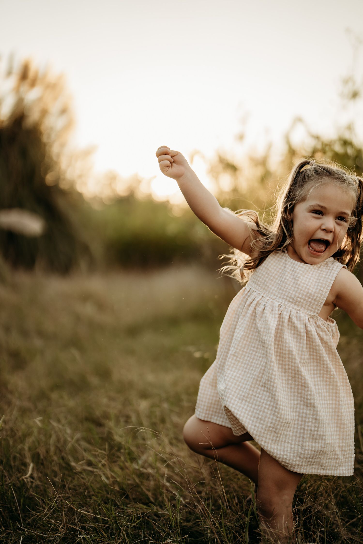 Young child in a white dress jumping joyfully outdoors at sunset.