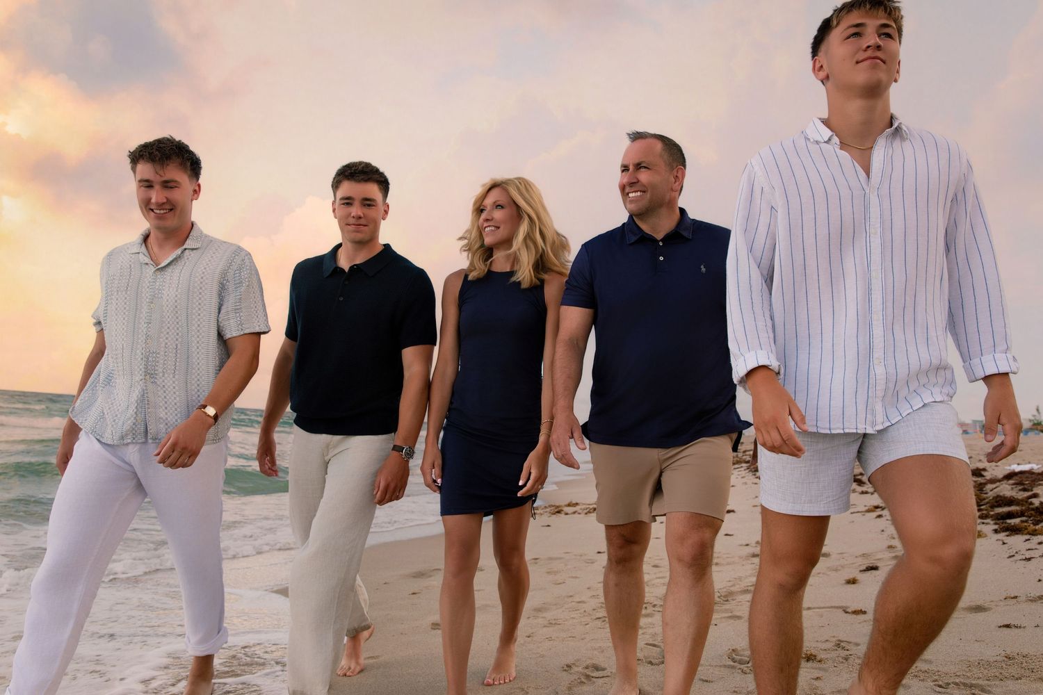 Large group enjoying sunset on beach wearing casual summer attire.