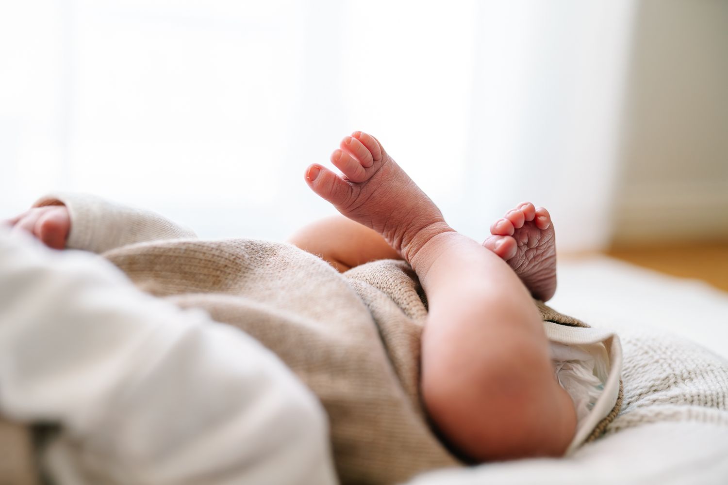 Close-up of a newborn baby's tiny feet and legs wrapped in a soft beige blanket on a white surface taken by Melbourne Newborn Photographer.