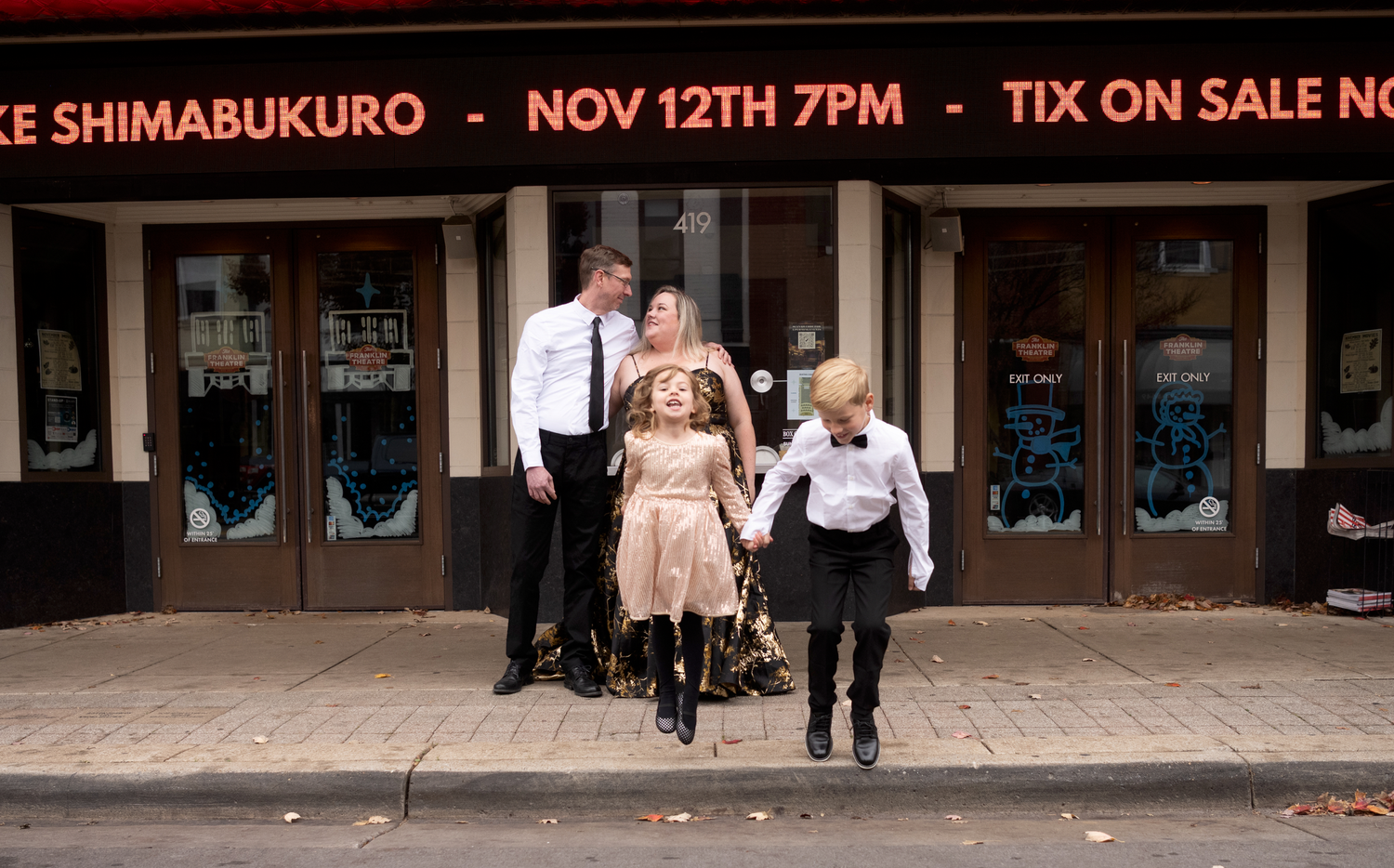 Three people pose outside a venue advertising Jake Shimabukuro on Nov 12th at 7PM with tickets on sale.