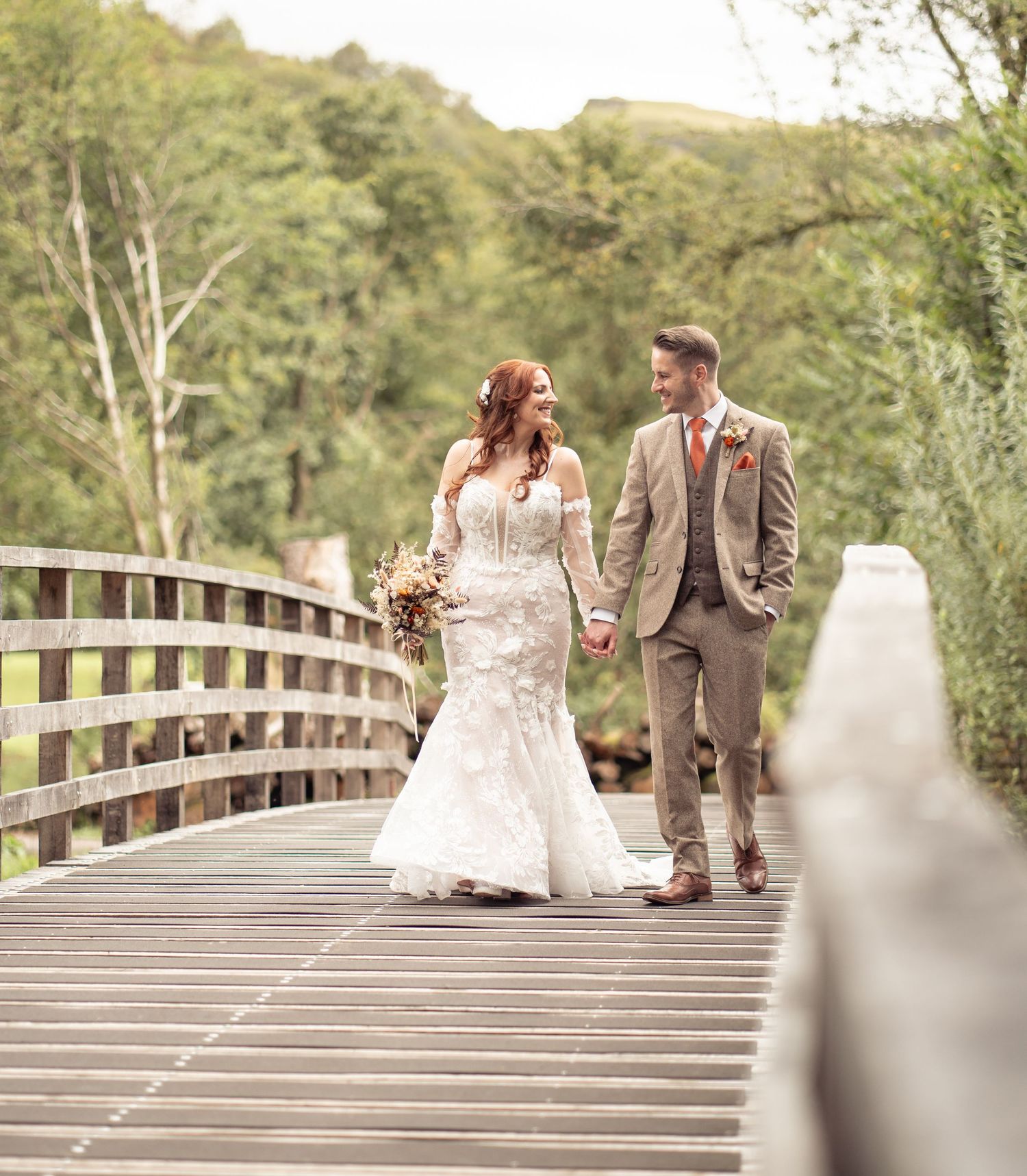 Couple sits together on wooden boardwalk surrounded by lush greenery on sunny autumn day.