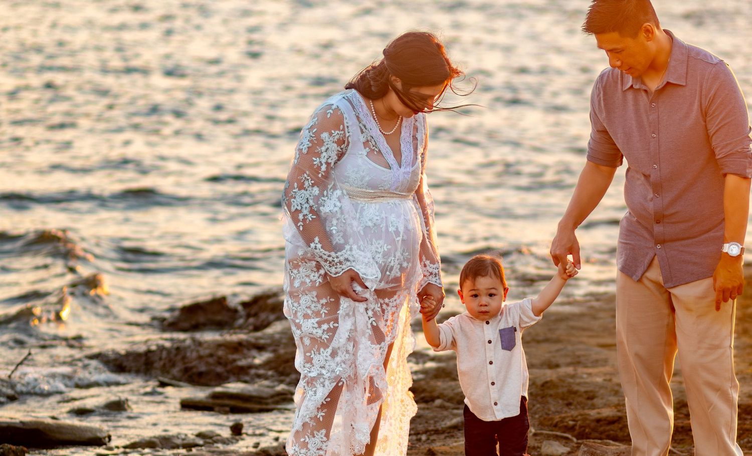 Family enjoying sunset together on rocky beach during maternity photoshoot.