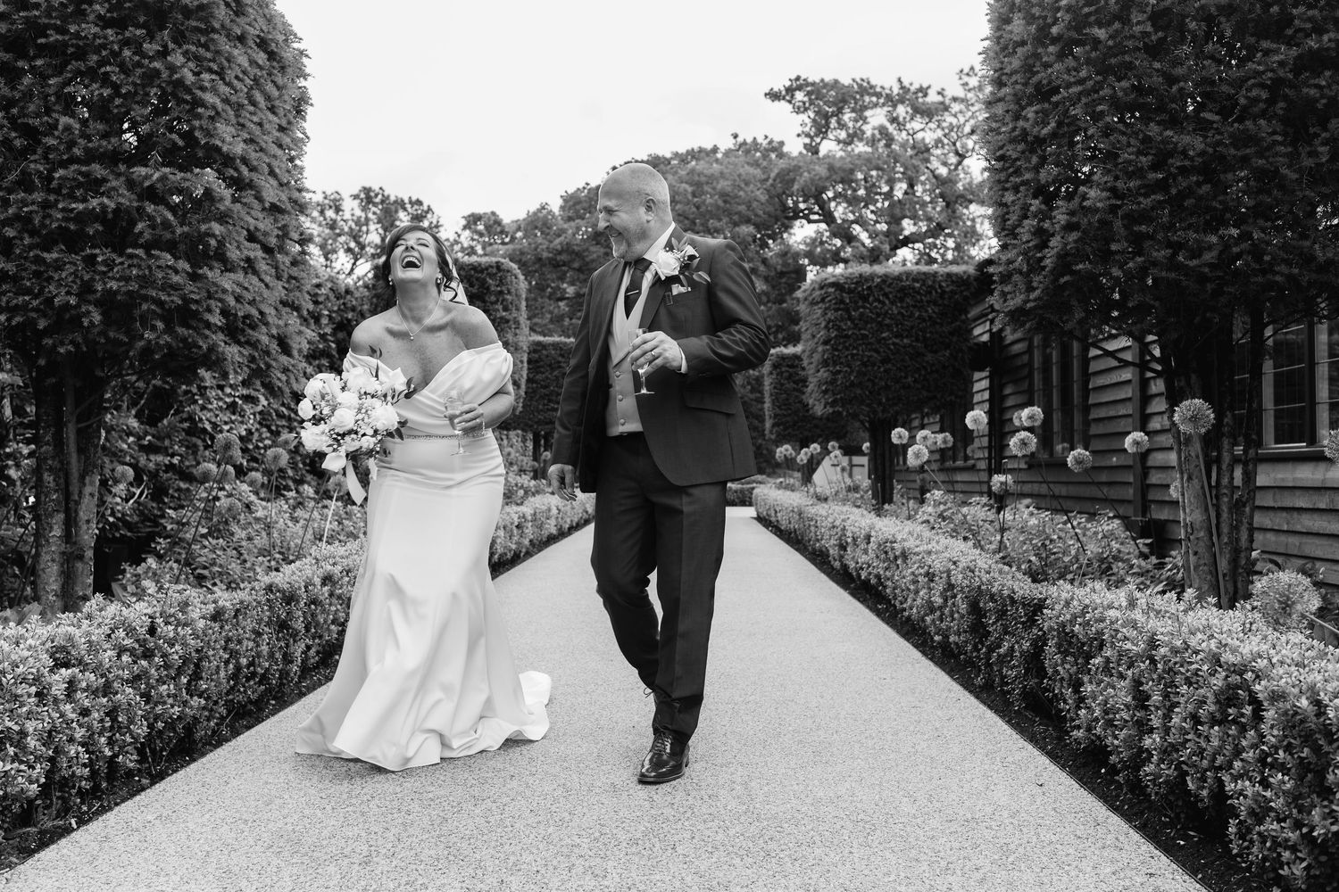 Happy couple walking and laughing together along a formal garden pathway.