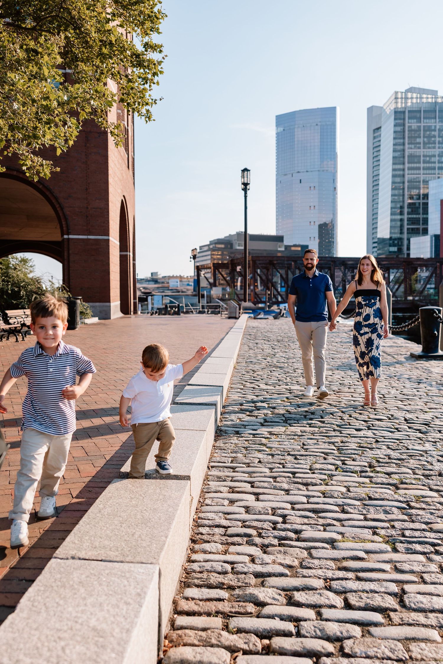 Stone brick walkway leading past historic buildings with modern skyscrapers visible in the background on sunny day.