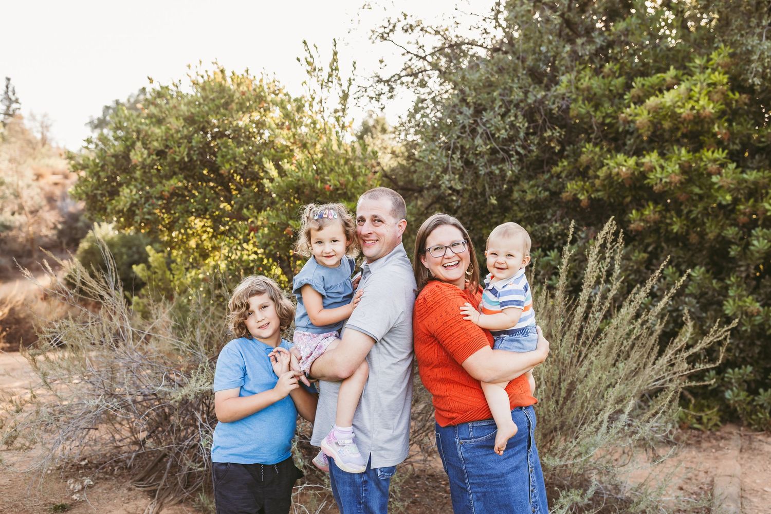 A group poses together outdoors in coordinating blue and orange outfits against a natural backdrop of trees and foliage.