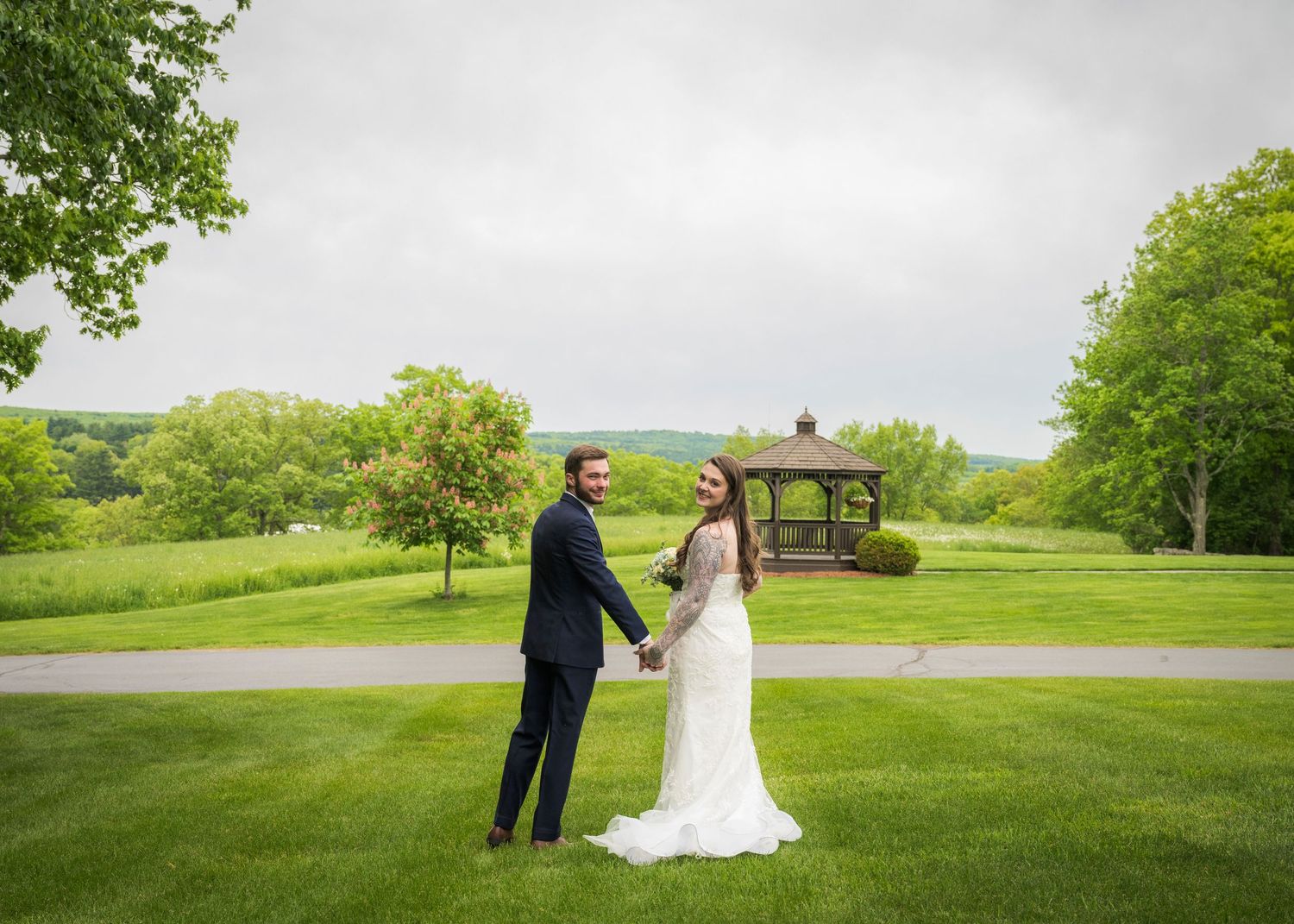 Newlyweds share an intimate moment outdoors with autumn foliage and rustic architecture in background.