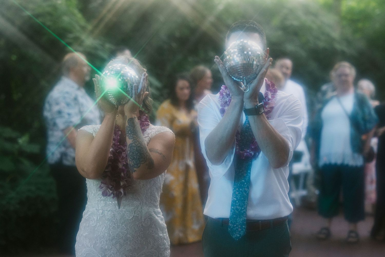 Wedding guests dance at an outdoor evening reception under string lights as flashes illuminate the celebration.