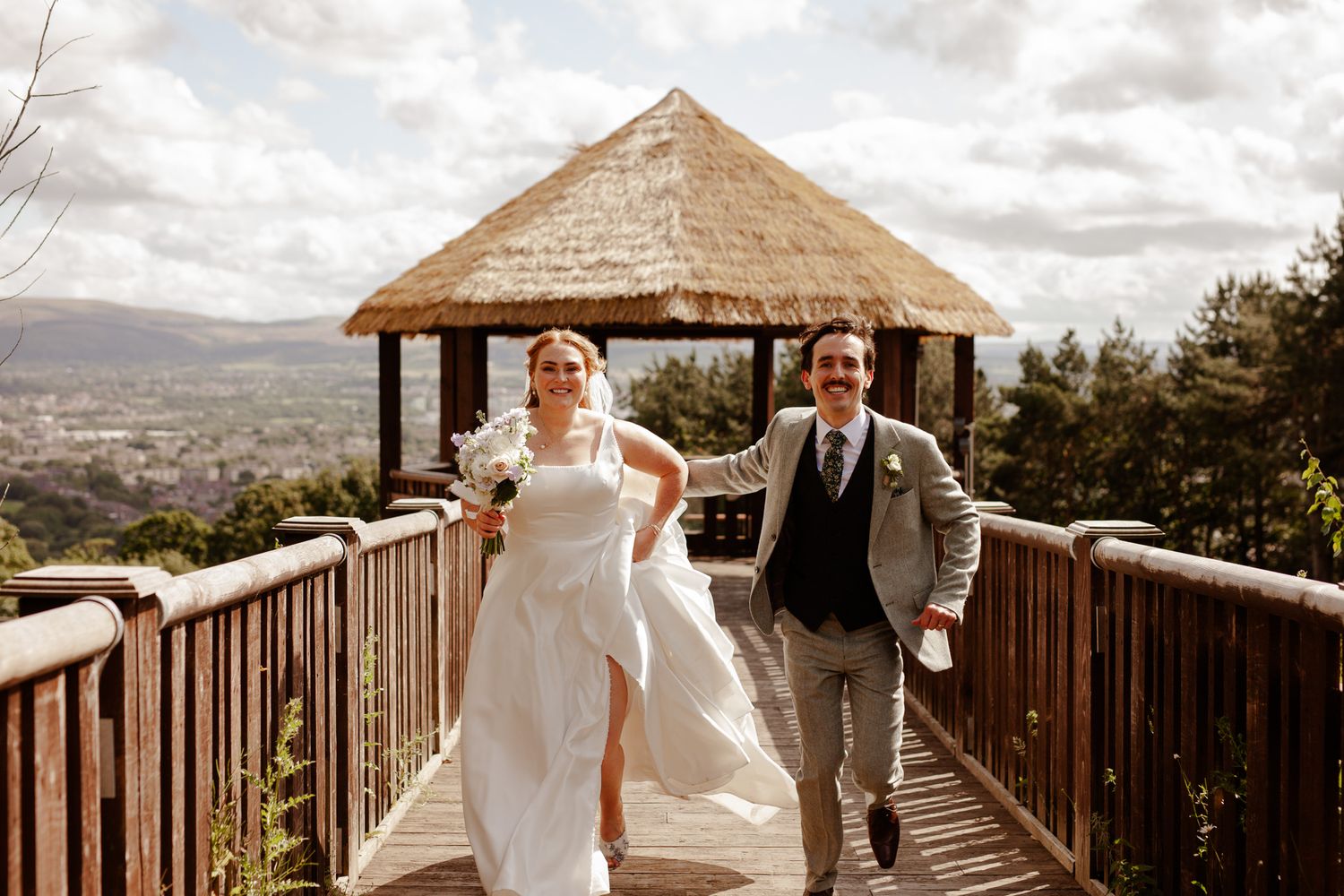 Couple celebrating on wooden observation deck with mountain vista in background.