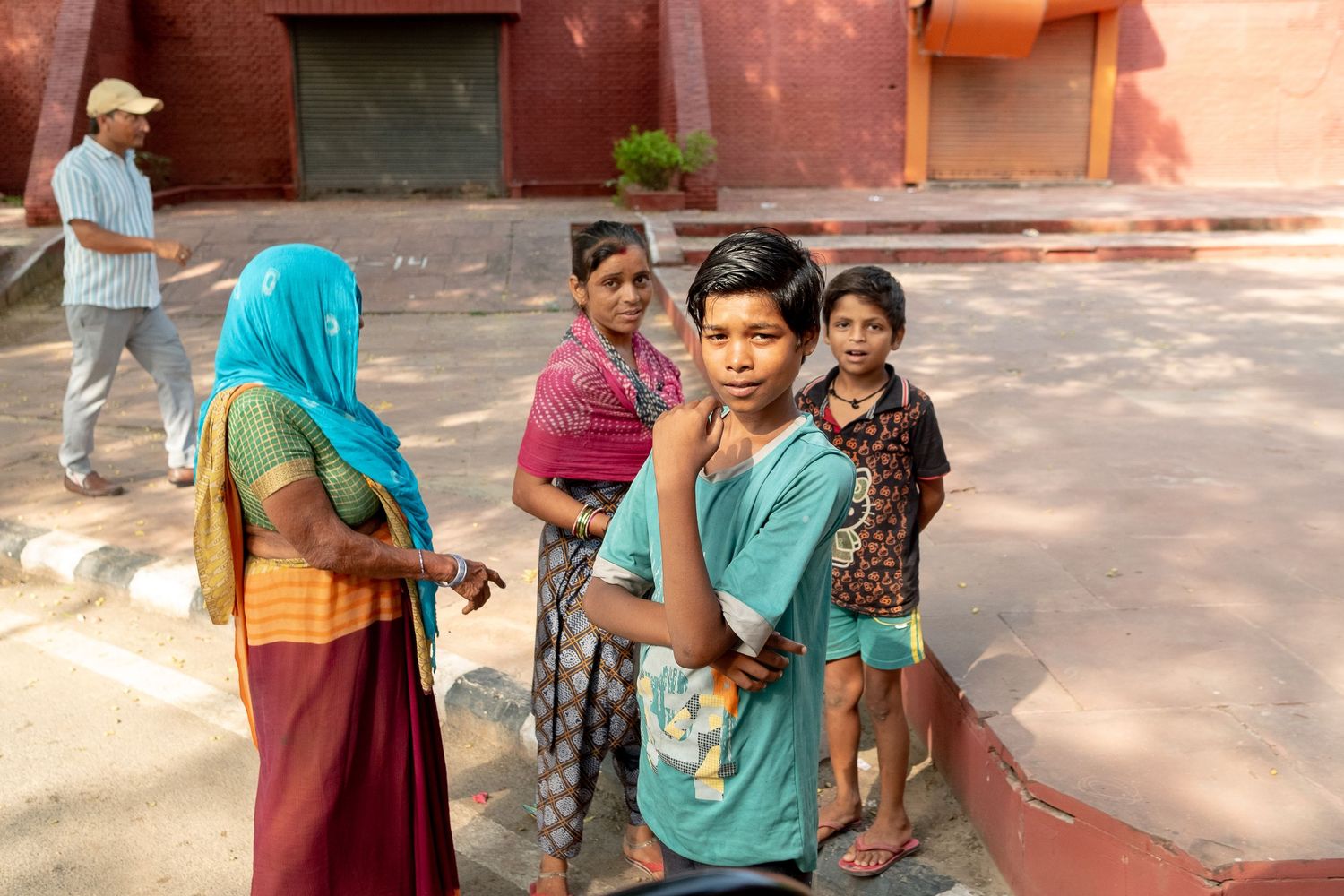 Courtyard scene with people gathered near red-painted buildings in bright daylight.