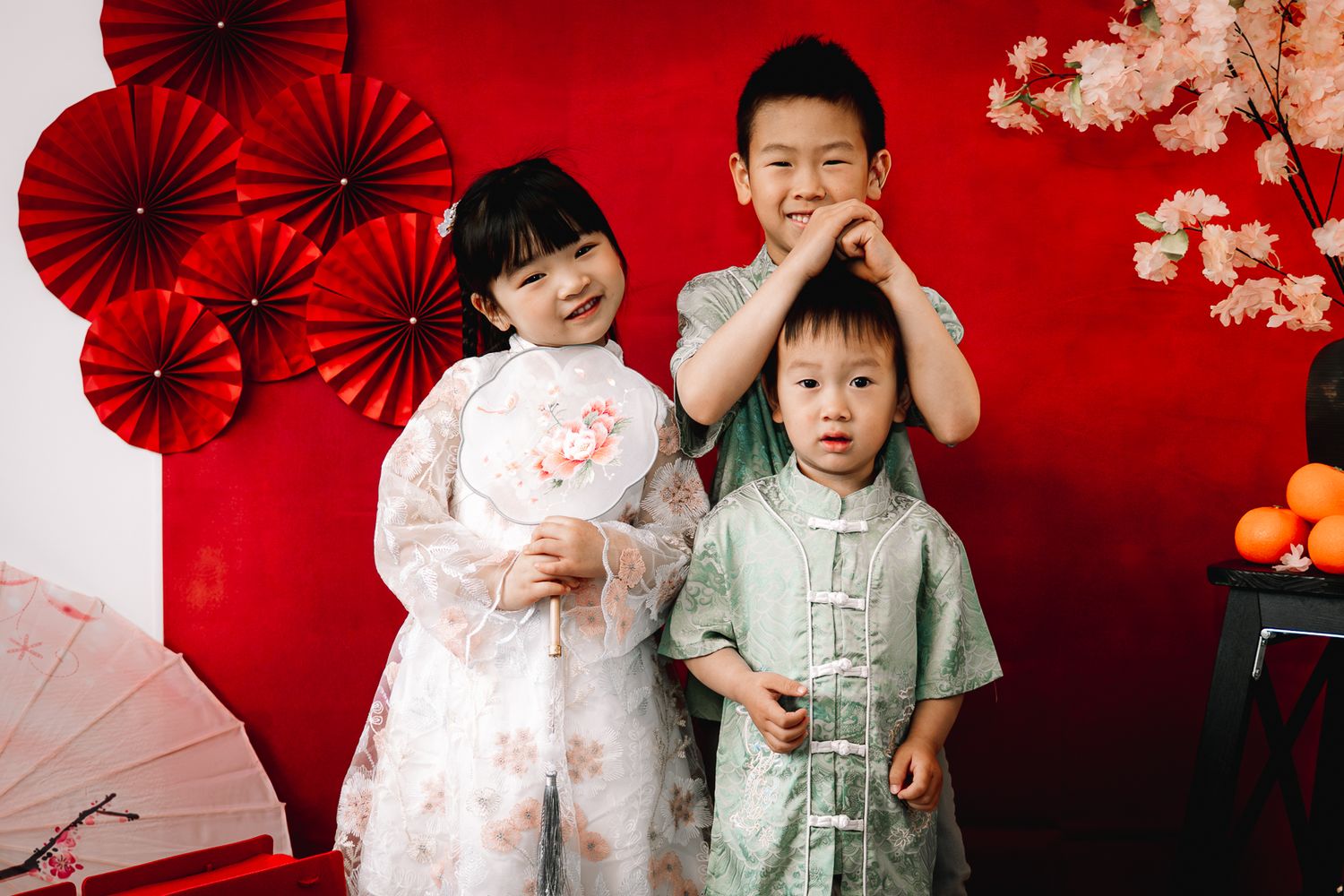 Children in traditional Chinese outfits pose against a red backdrop during a Melbourne Chinese New Year Mini Photo Session