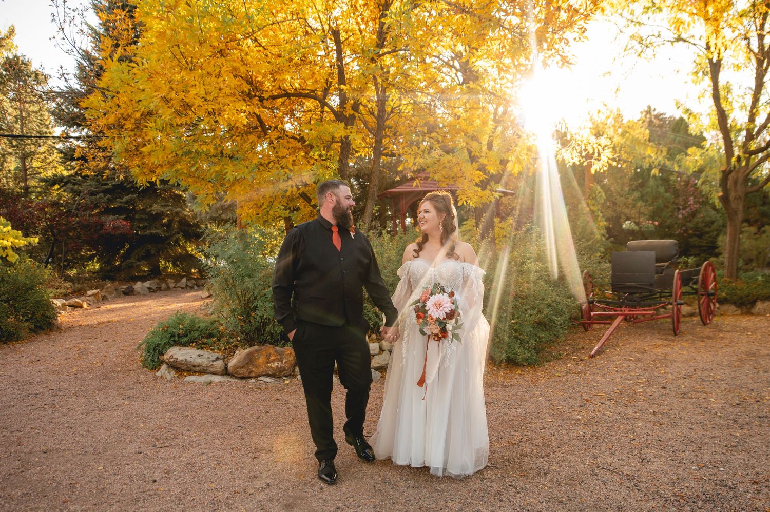 A couple walks hand in hand through a golden autumn forest path with sunlight streaming through the trees.
