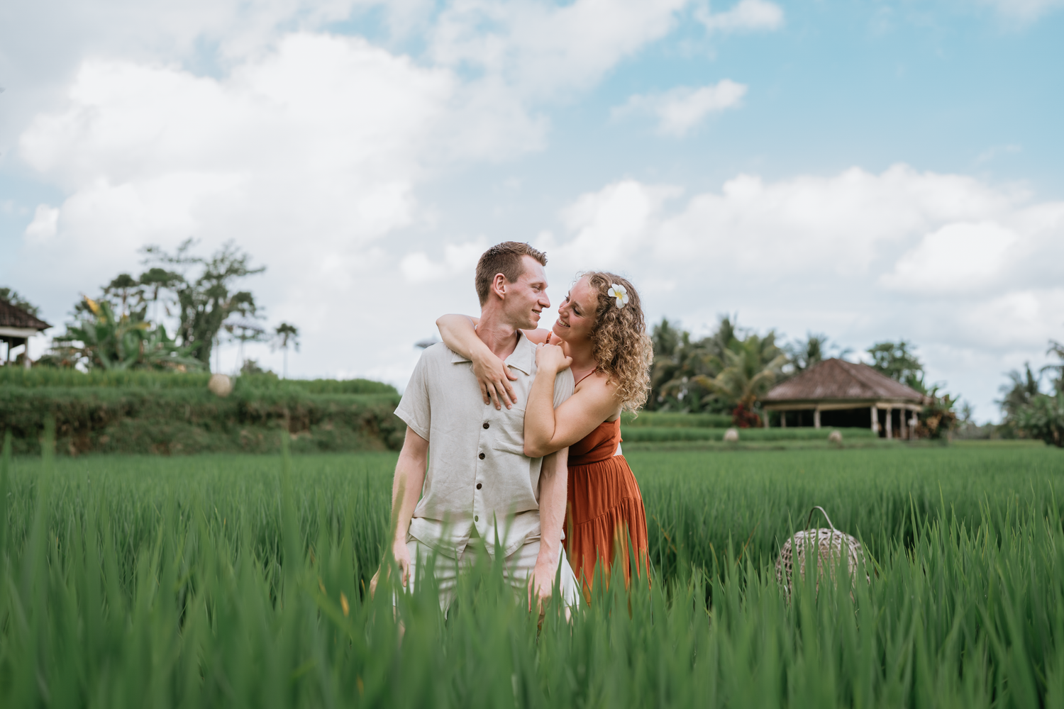 Couple enjoying views from elevated wooden deck with traditional Balinese statues in background.
