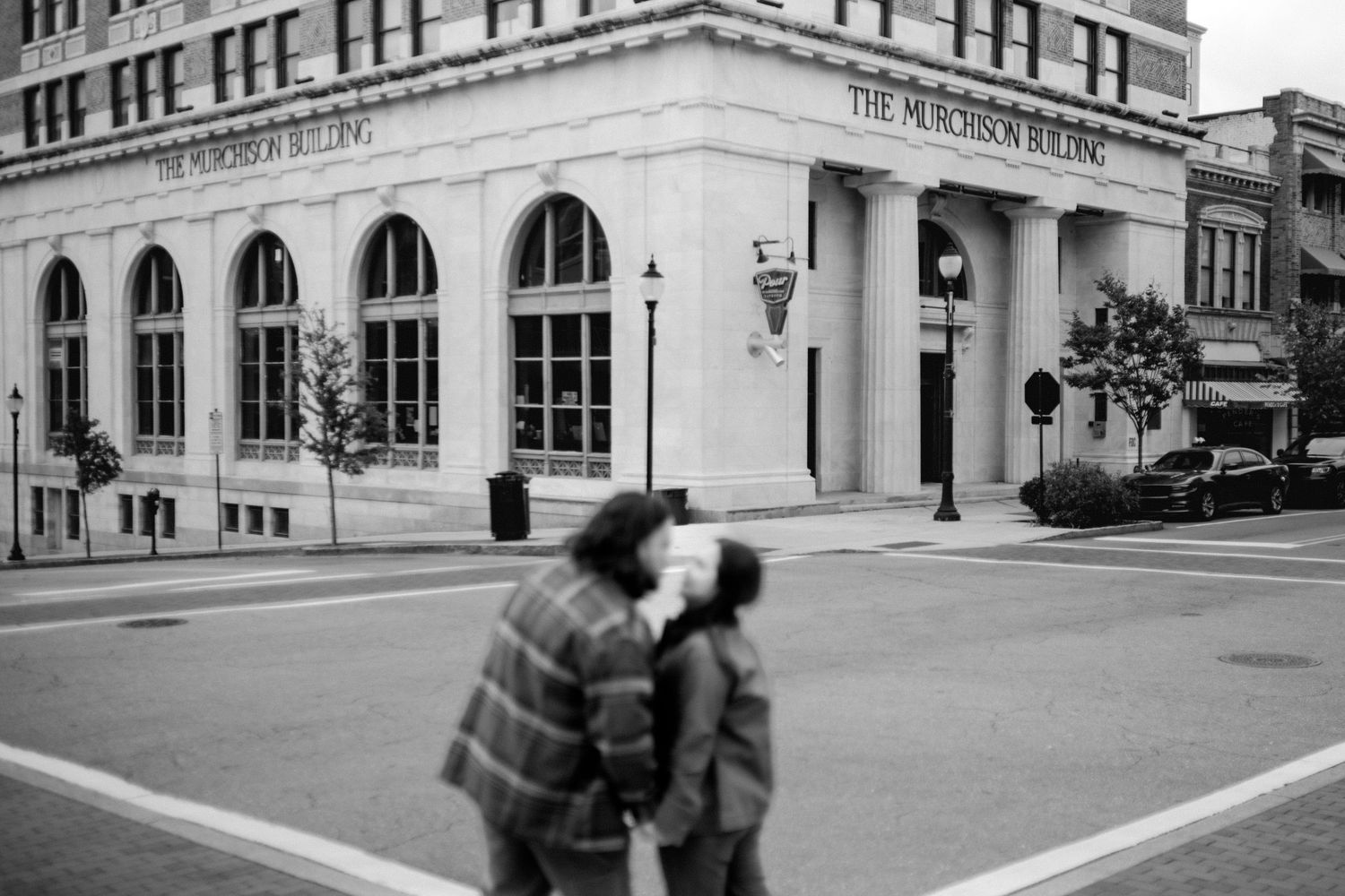A black and white photo shows a couple dancing together in front of a grand historic building with arched windows.