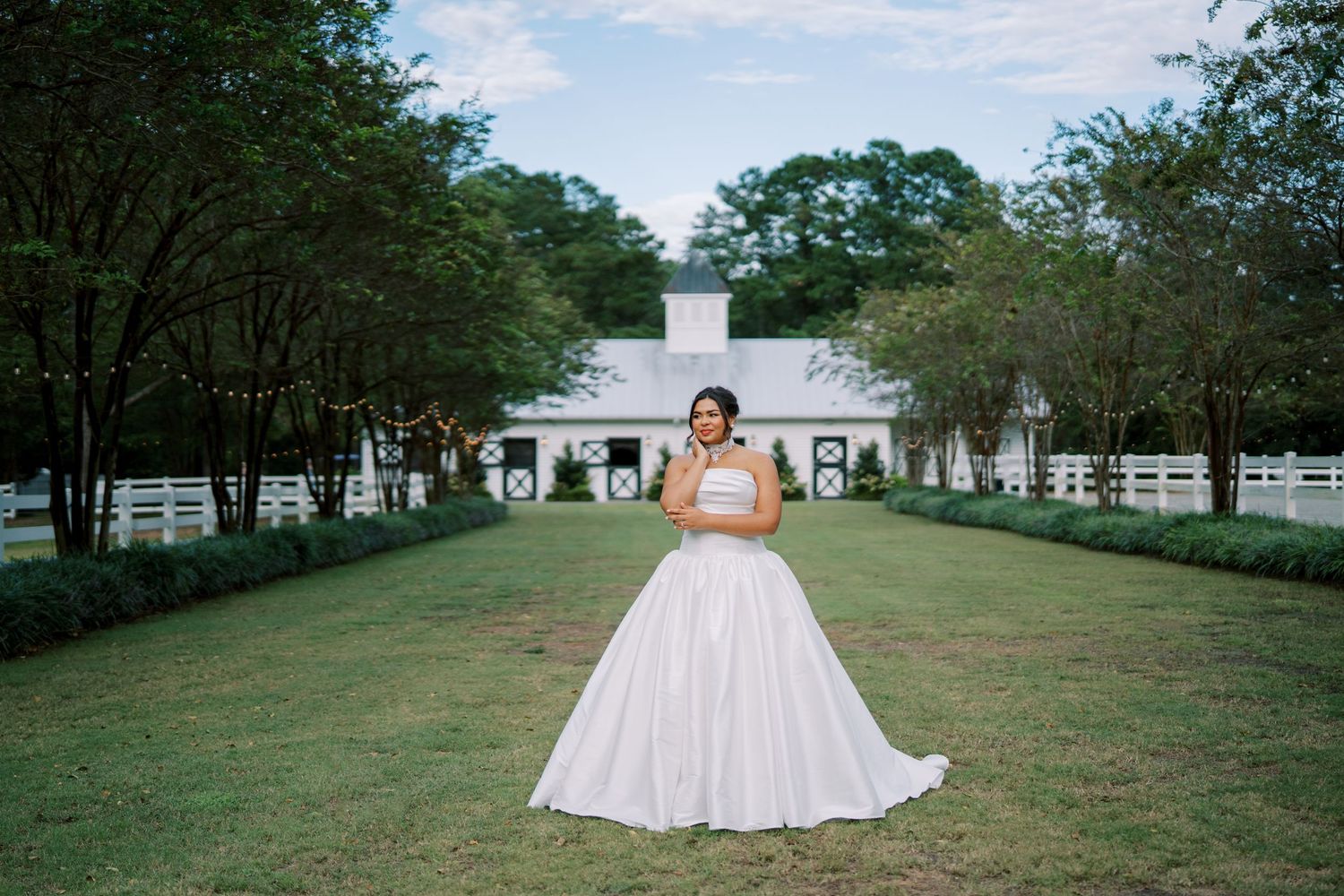 A bride in a flowing white ballgown poses in various spots around a scenic outdoor venue with white buildings and green lawns.
