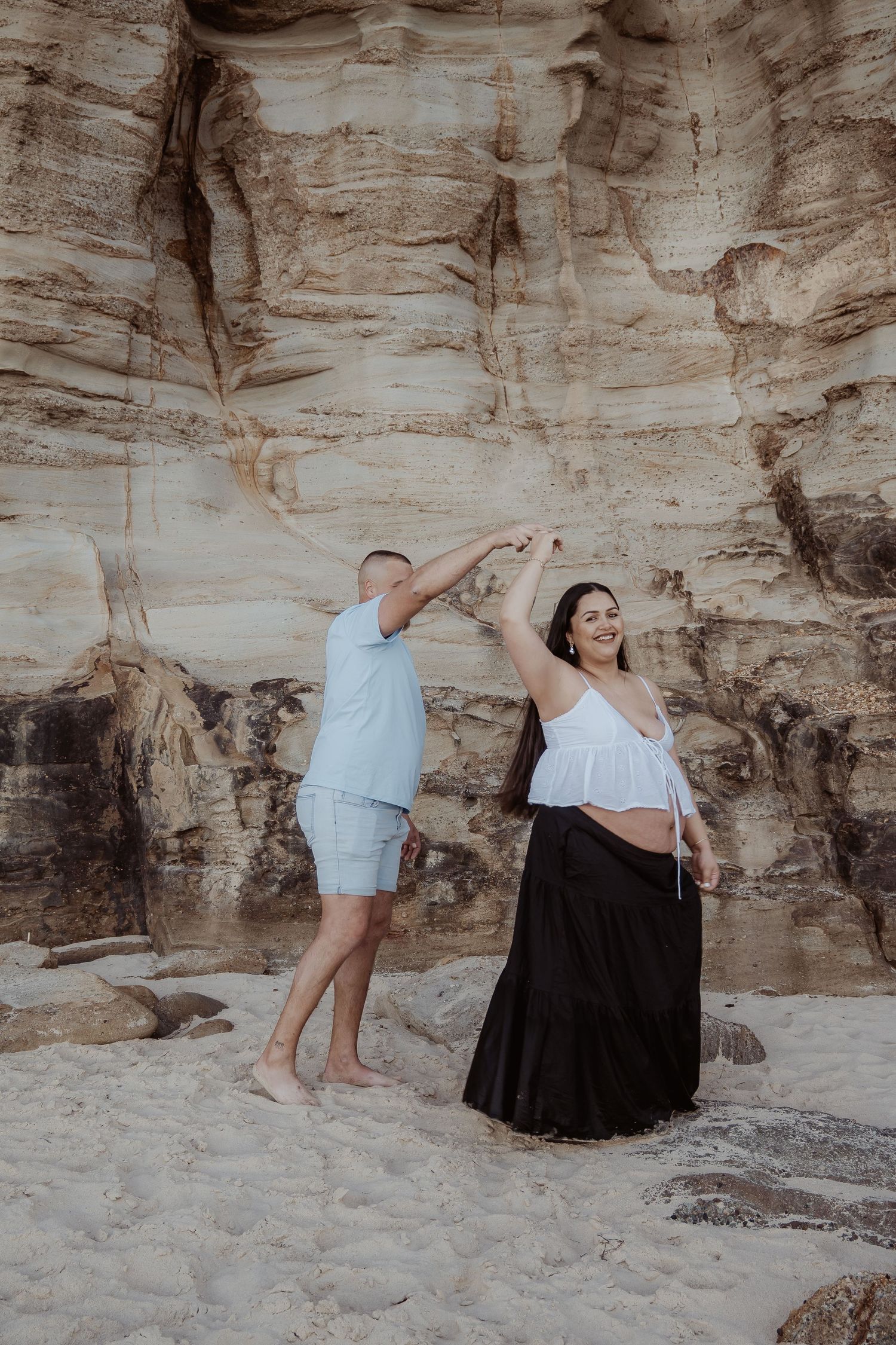 A series of artistic poses captured against a textured rock wall in a desert landscape at sunset at a central coast maternity photoshoot.