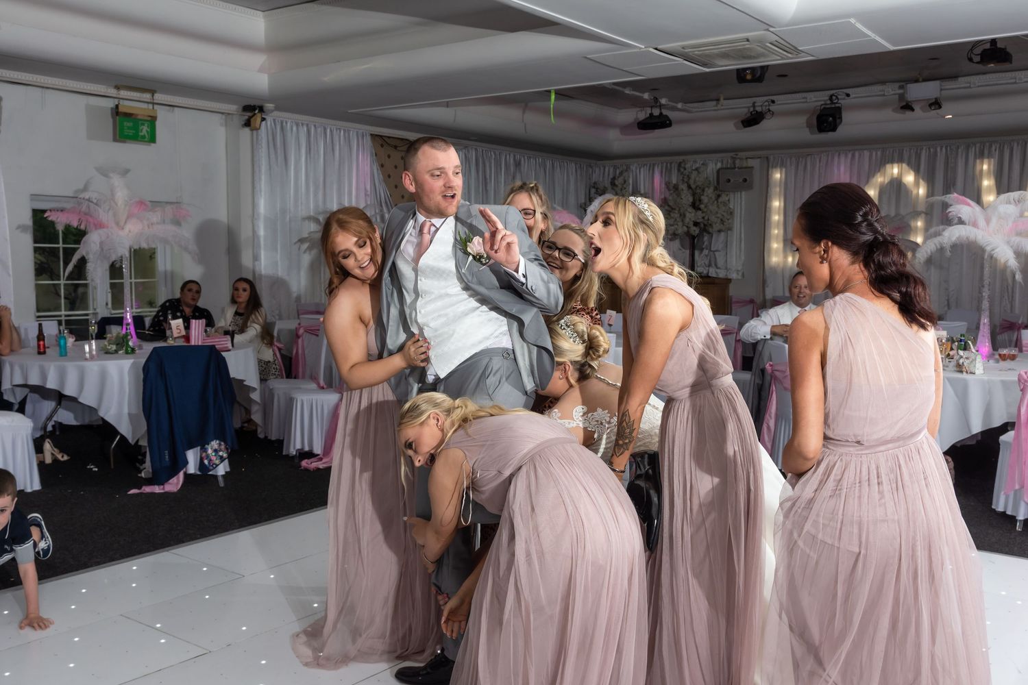 Wedding party celebrates on the dance floor with bridesmaids in dusty rose dresses during a festive reception.