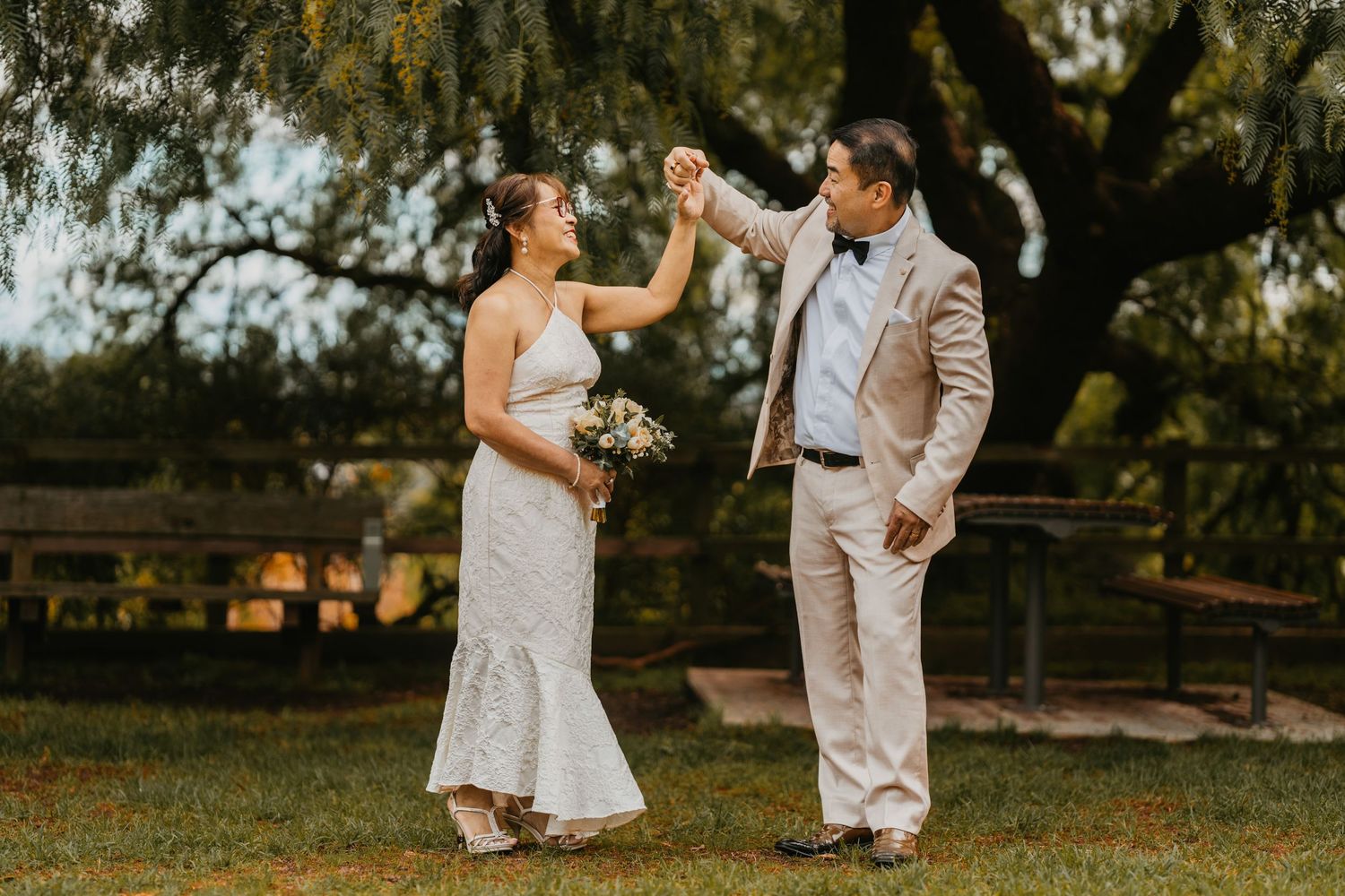 Wedding couple dances together in a sun-dappled garden during golden hour celebration.
