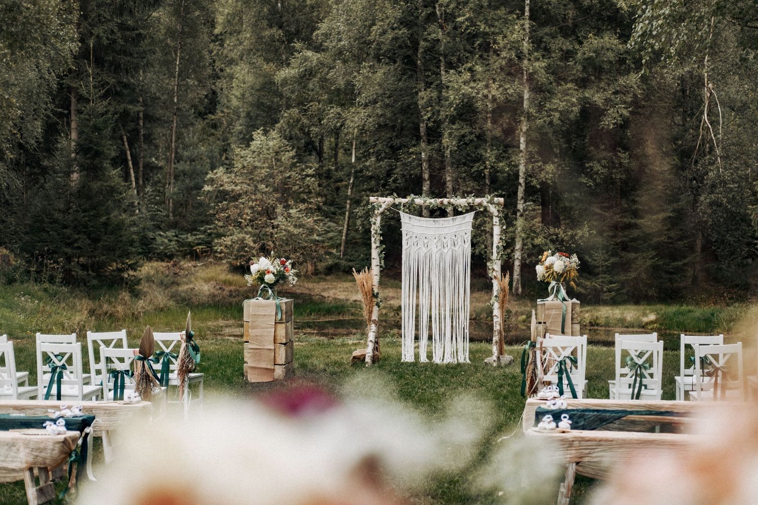 Outdoor wedding ceremony setup with white chairs and floral decorations in a forest setting.