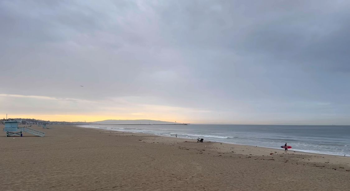 A serene coastal panorama shows a misty beach landscape with scattered figures walking along the shoreline at dusk.