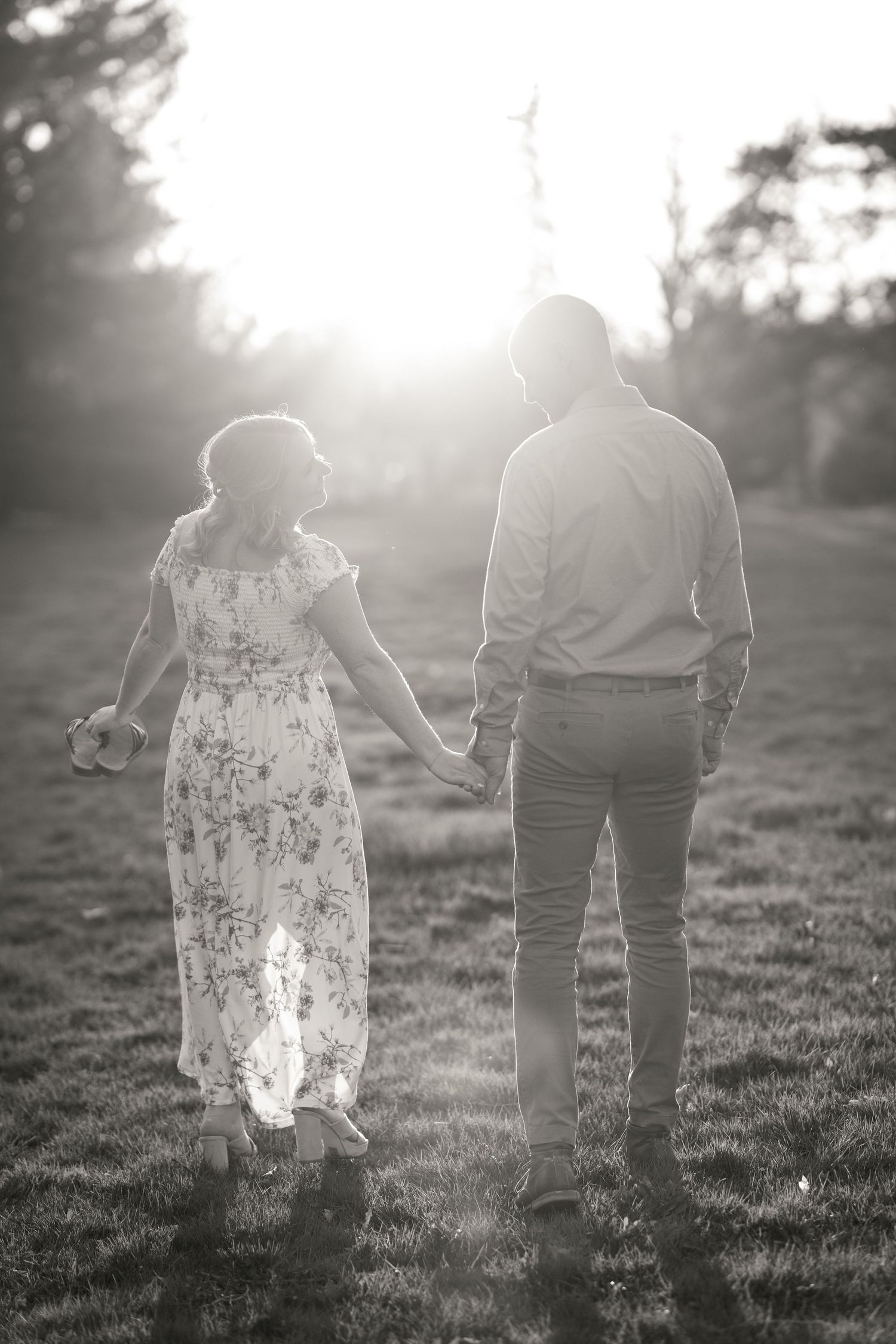 A couple holding hands walks away into sunlit field with backlit silhouettes and dreamy atmosphere. Ottawa Wedding Photographer Tim Gowling