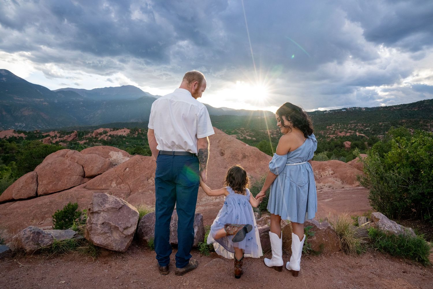 Family enjoying sunset together at Garden of the Gods park in Colorado with dramatic cloudy sky and red rocks.