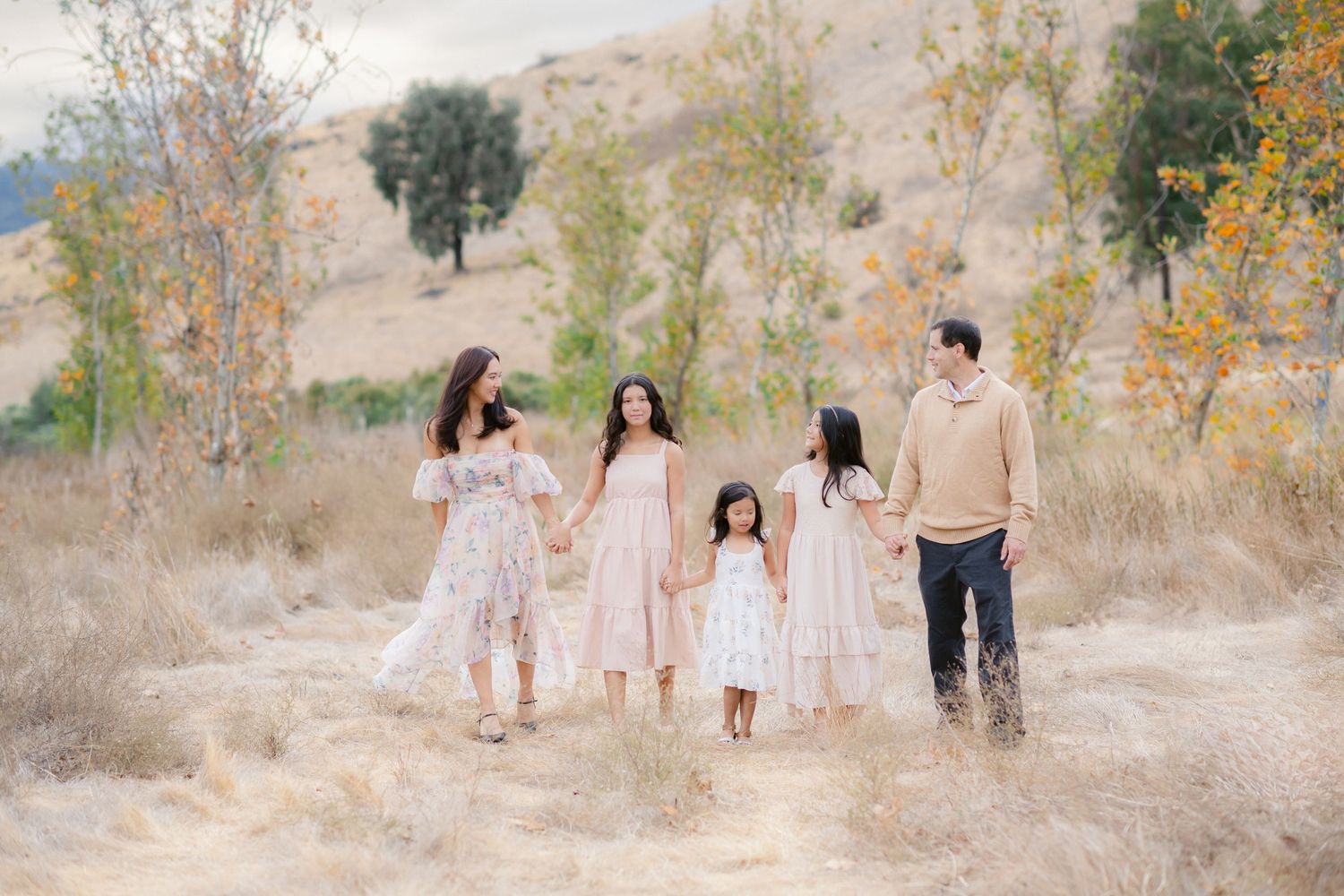 A group wearing coordinated blue and white outfits poses together in a sunlit garden setting for family photos.