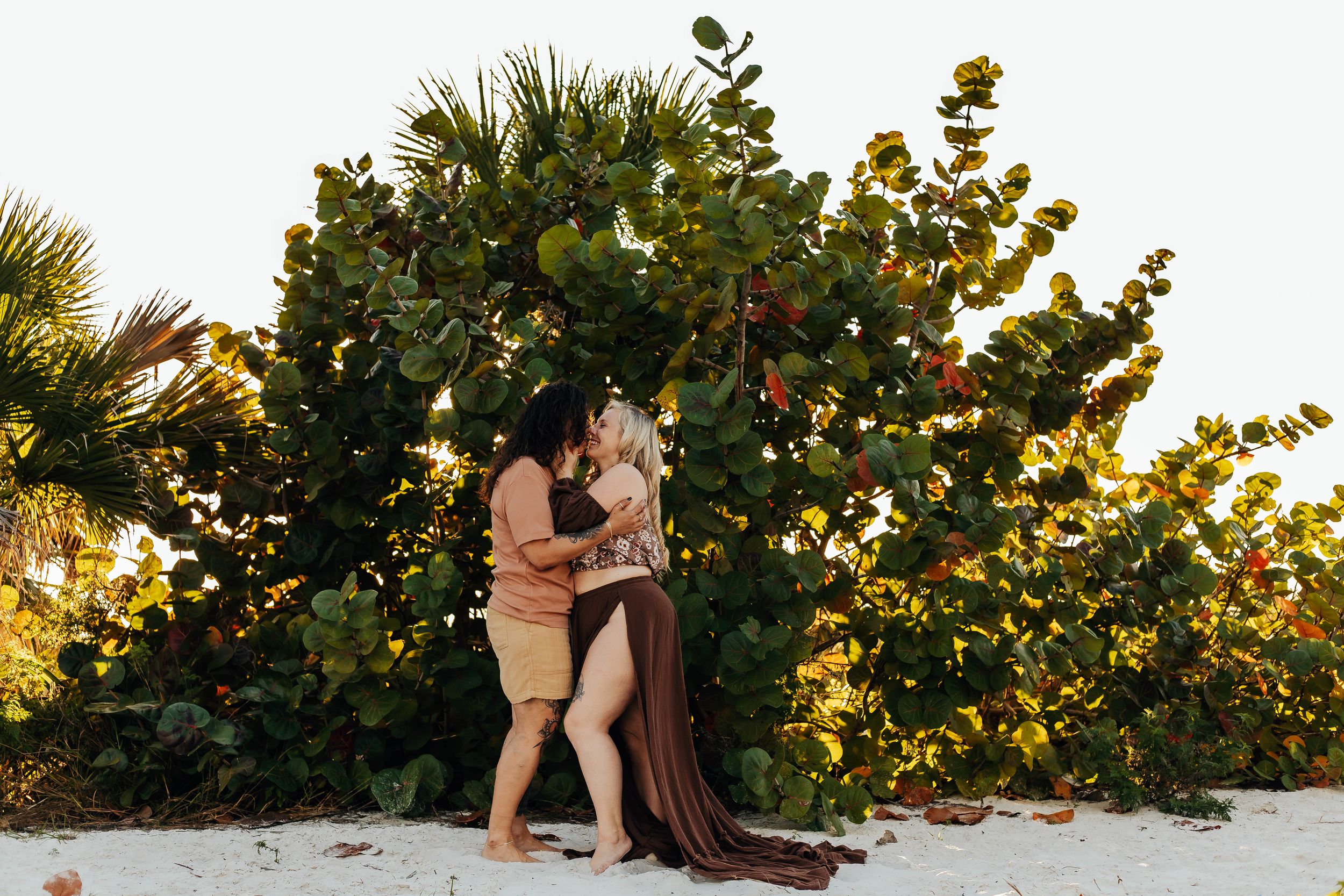 A romantic beach proposal scene at sunset with sea grape trees in the background.