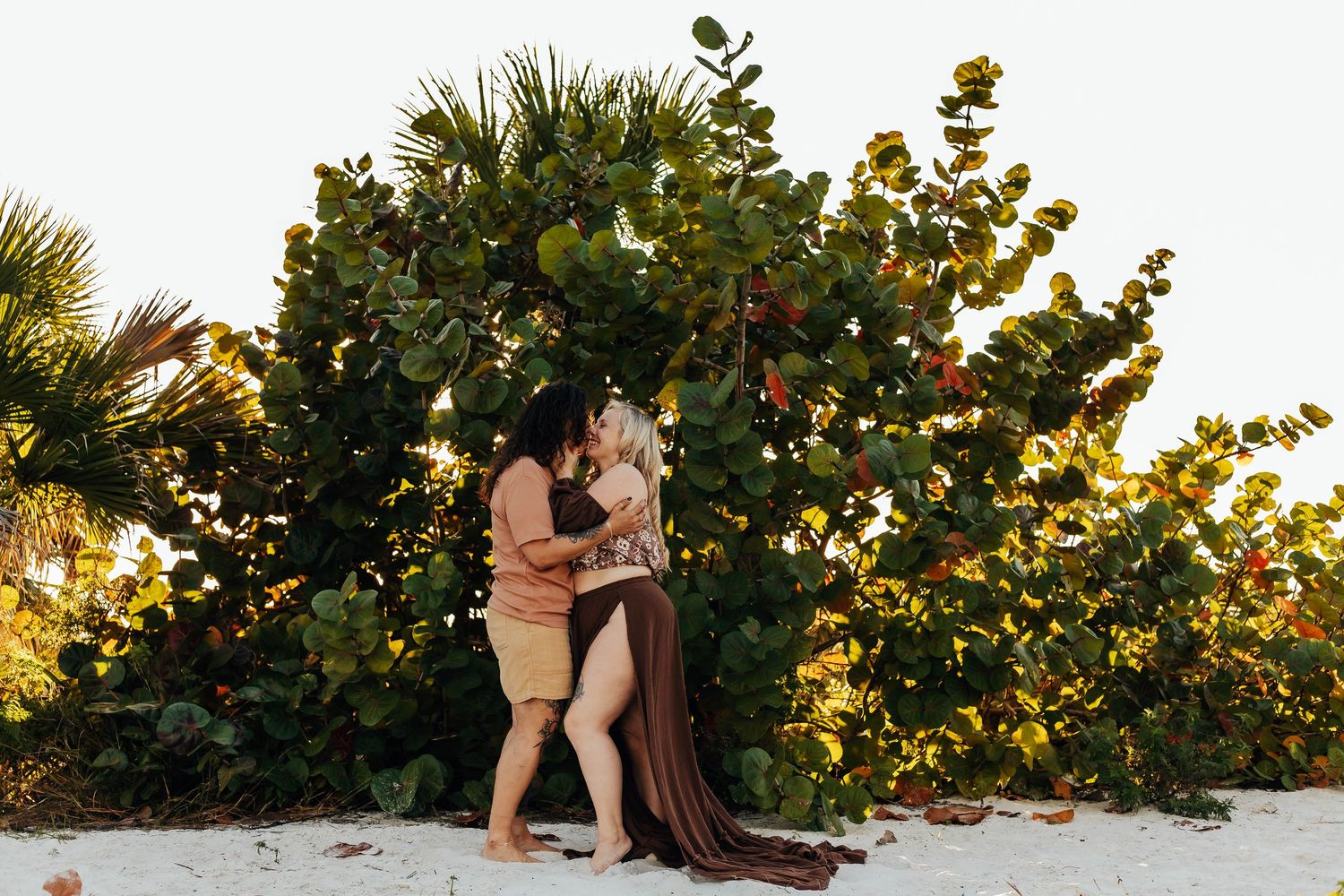 A romantic beach proposal scene at sunset with sea grape trees in the background.