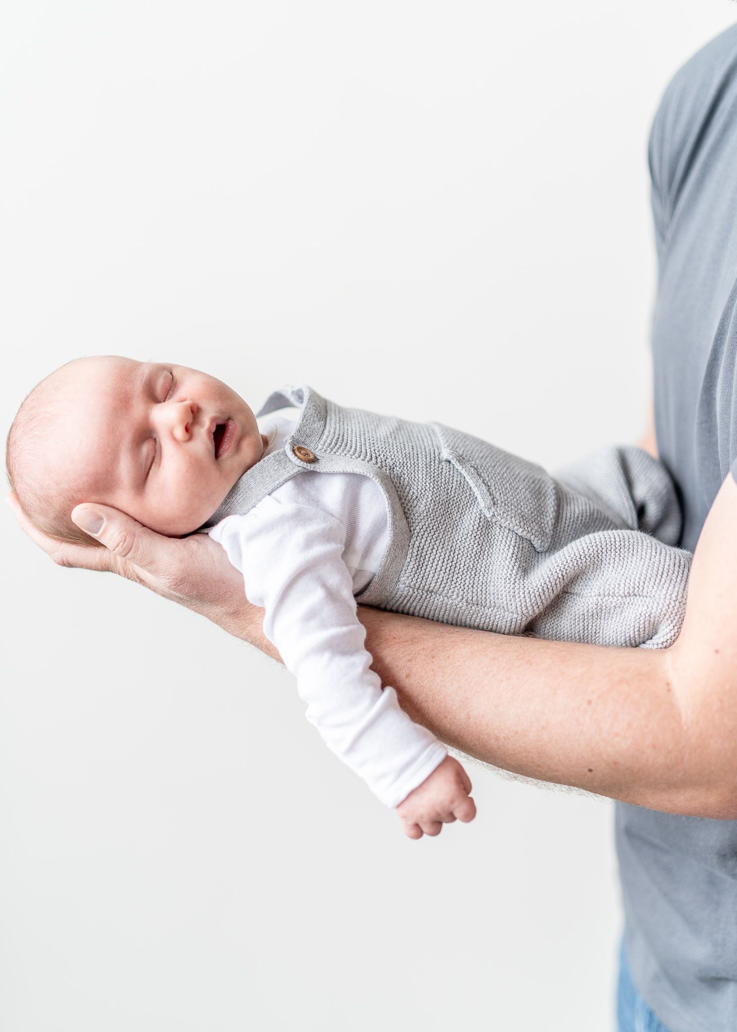 A baby wearing a white onesie sleeps peacefully while being cradled in someone's arms.