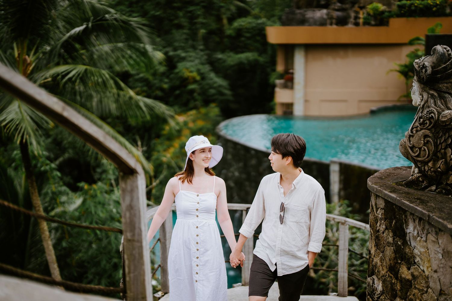 A couple walks down stone steps in a lush tropical garden setting.