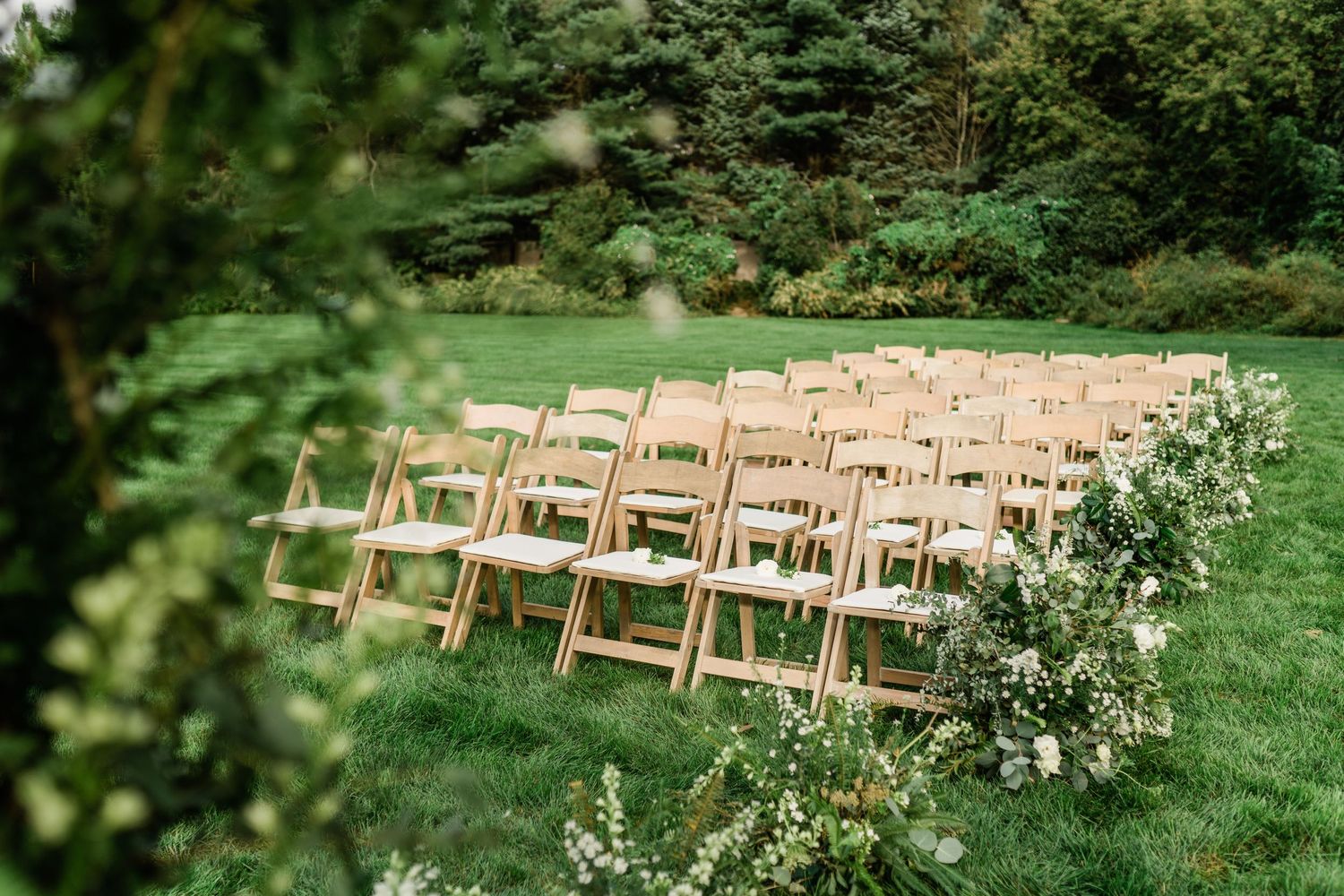 Rows of wooden chairs set up for an outdoor garden wedding ceremony.