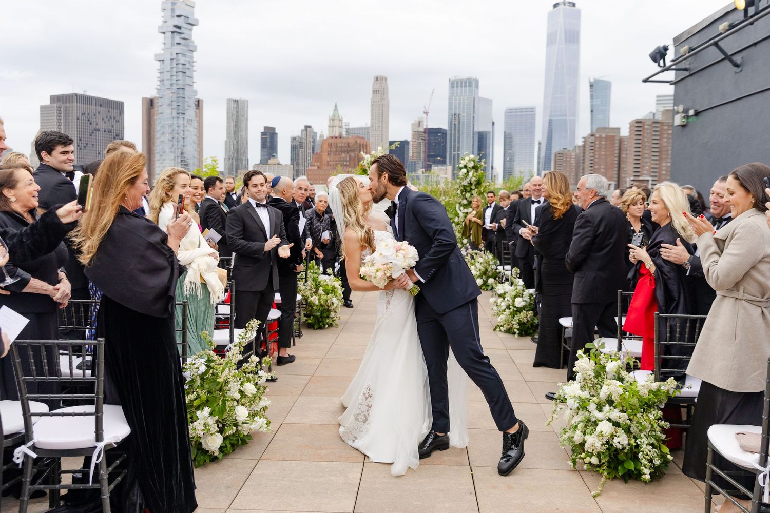 Rooftop wedding ceremony in New York City with Manhattan skyline views and floral arrangements along the aisle.