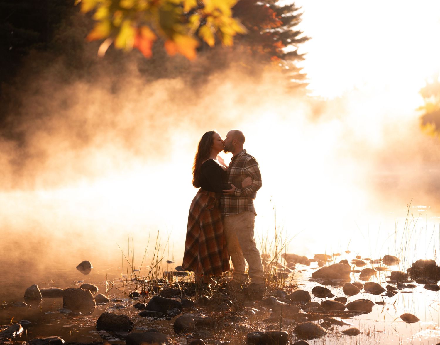 Silhouetted figures by water at golden hour with atmospheric mist and sunlight.