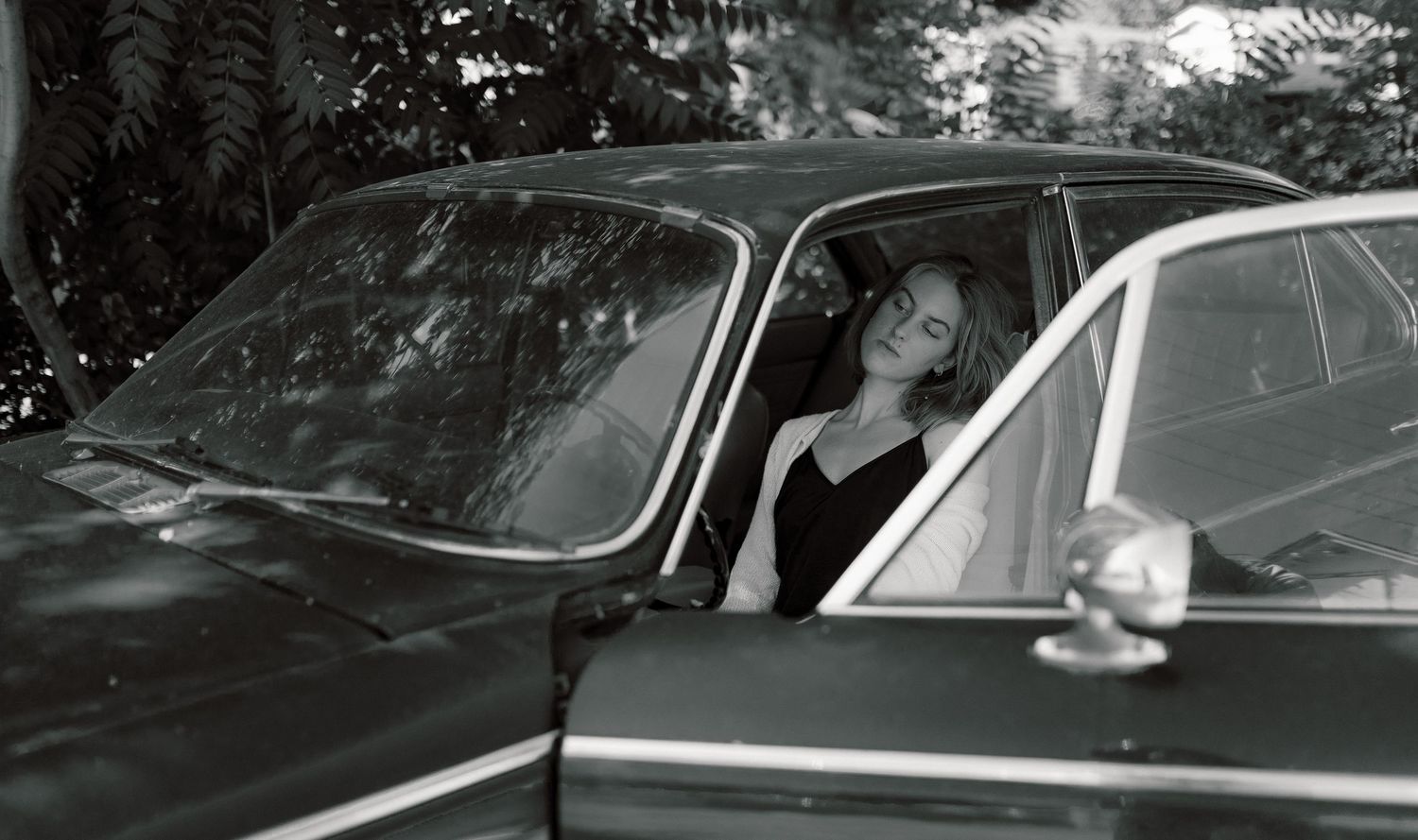 Black and white vintage photograph showing someone seated in a car with open windows.