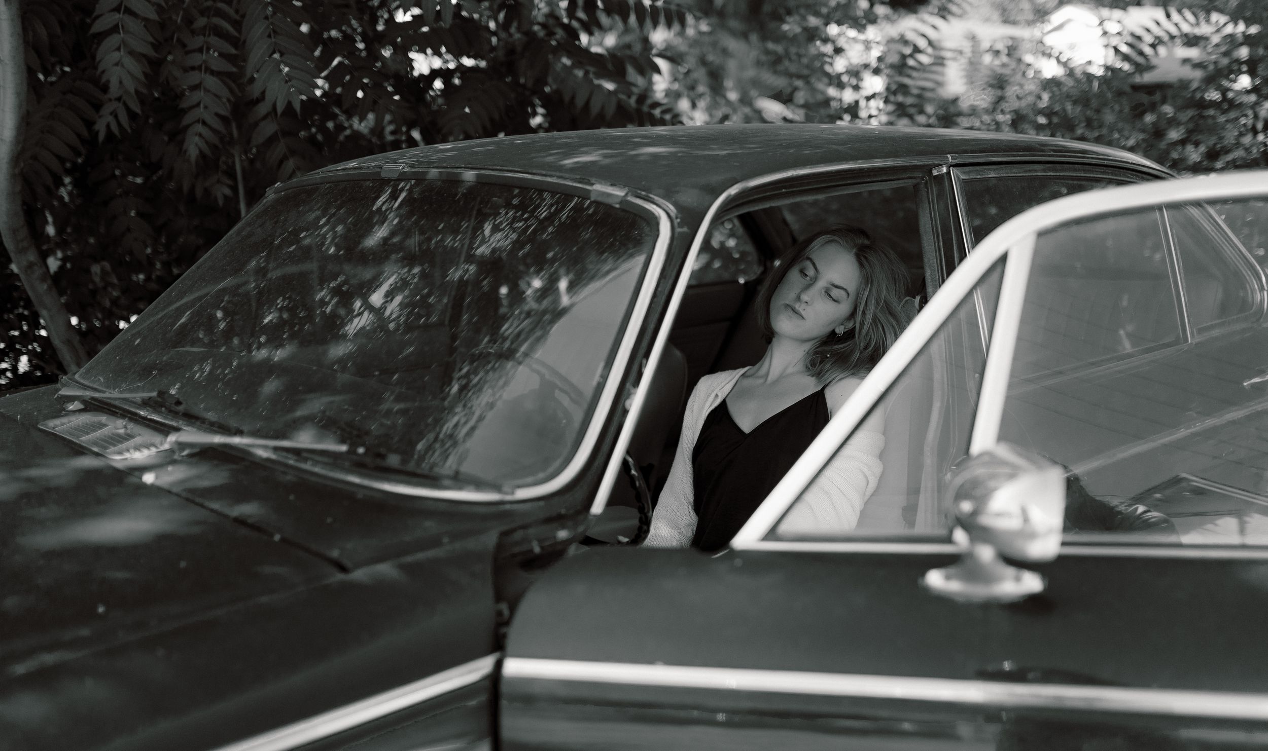 Black and white vintage photograph showing someone seated in a car with open windows.