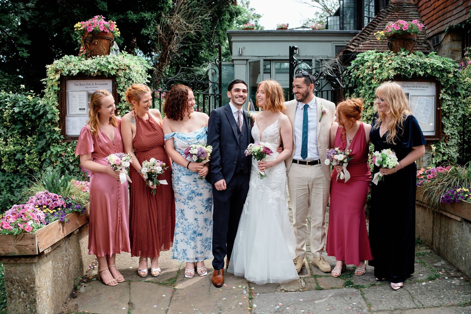 A celebration at a garden venue with bridal party members gathered together in coordinated dresses among blooming flowers.