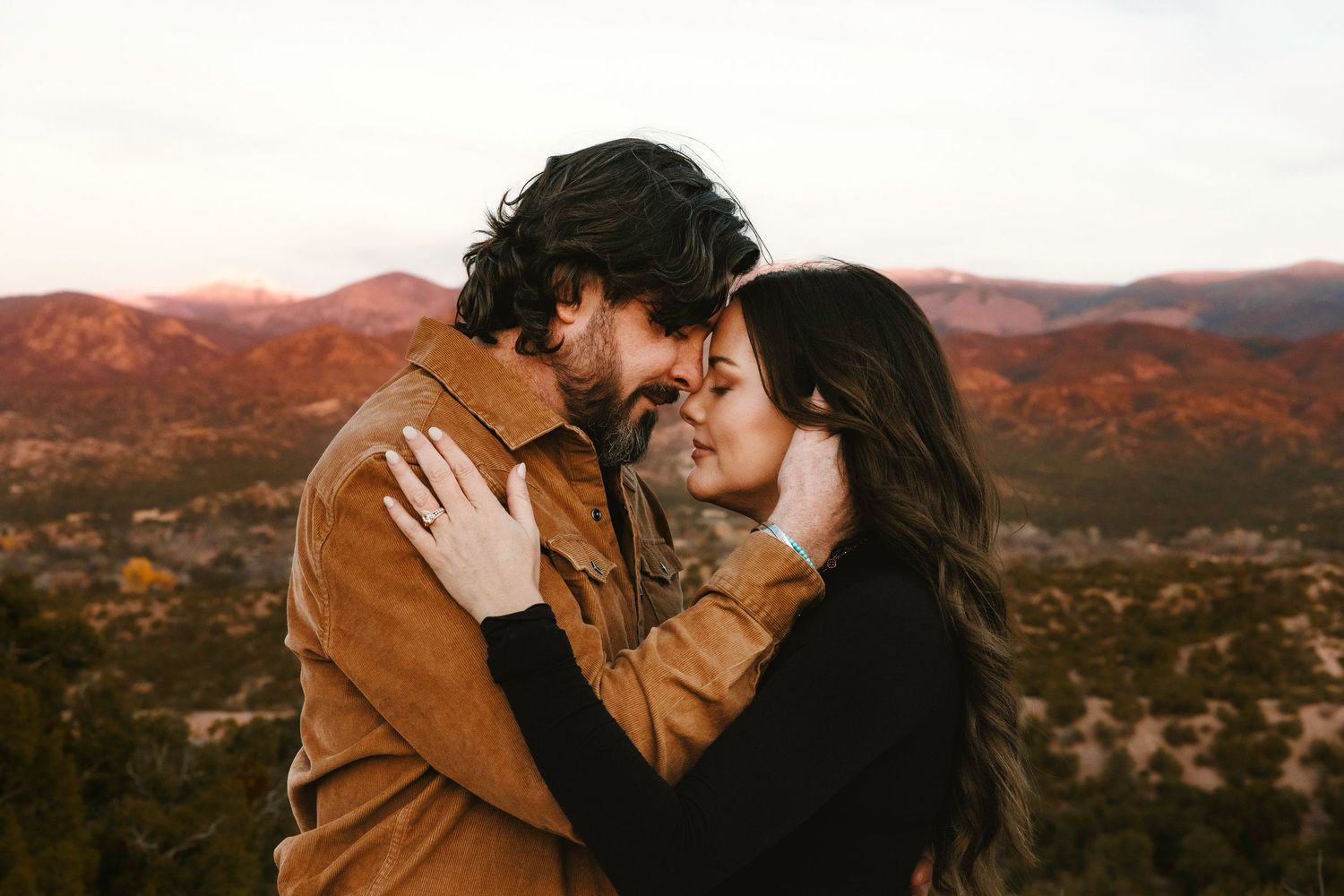 Romantic couple embracing at sunset with colorful autumn mountains behind them.
