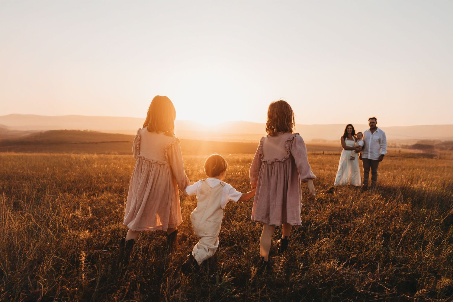 Silhouettes of people standing in golden field at sunset with warm sunlight streaming through.