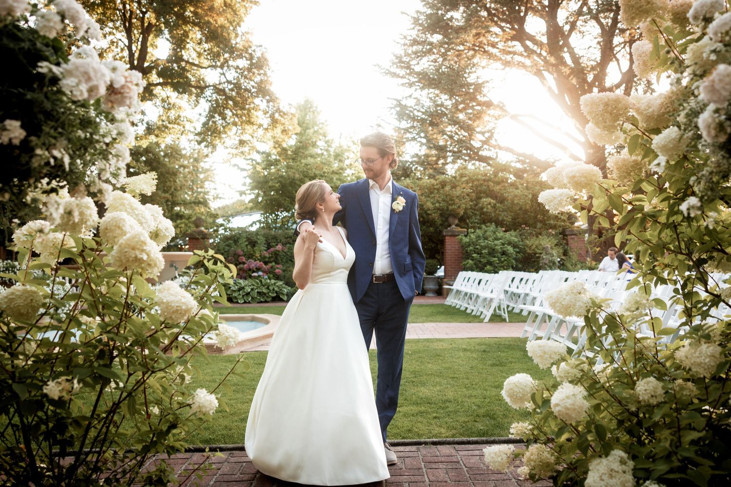 A romantic sunset wedding photo session in a garden with white hydrangea flowers blooming in the foreground.