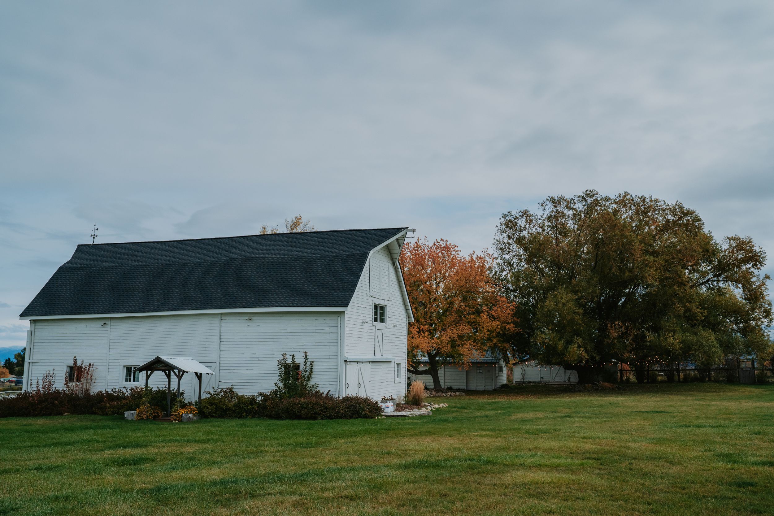 A panoramic view of white farm buildings and barns scattered across rolling green hills under a cloudy sky.