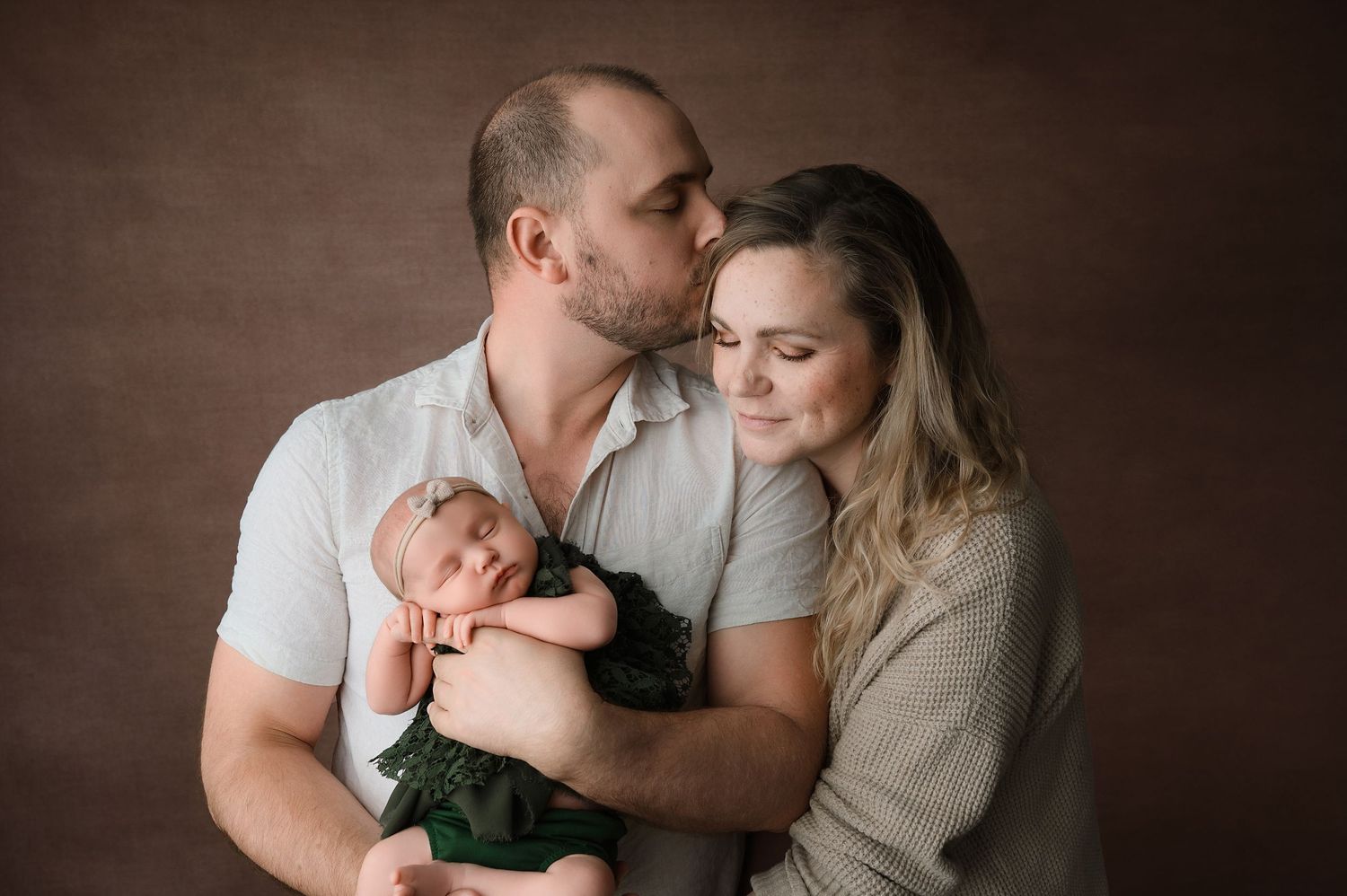 Six connected photos show intimate moments of a couple holding a newborn baby against a dark brown backdrop.