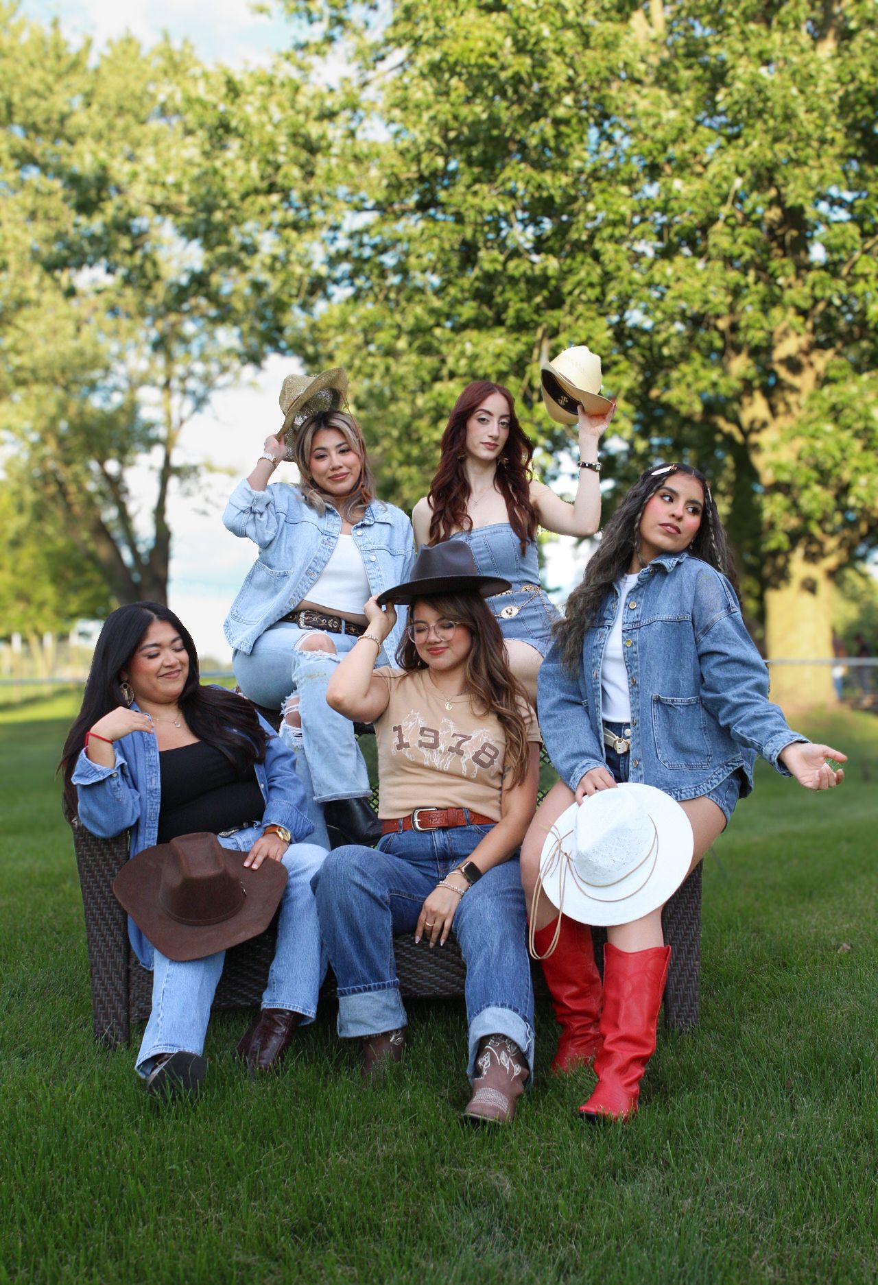 Friends in western wear and cowboy hats pose together on grass for group photo.
