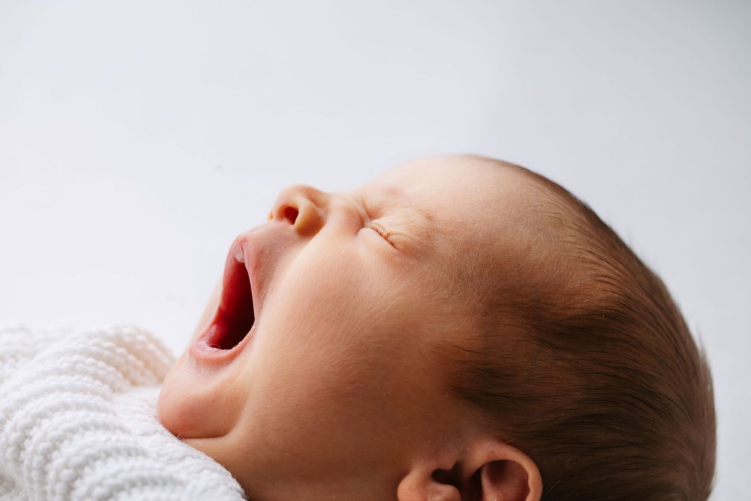 Baby wearing blue striped outfit lies on wooden floor with rustic backdrop.