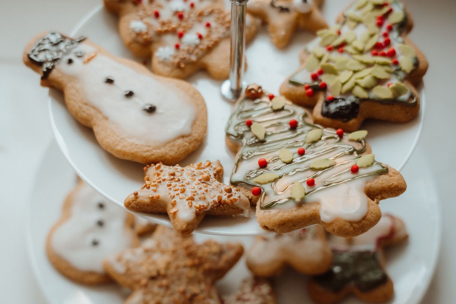 Festive decorated Christmas cookies including gingerbread figures and trees with icing and sprinkles on a white plate.