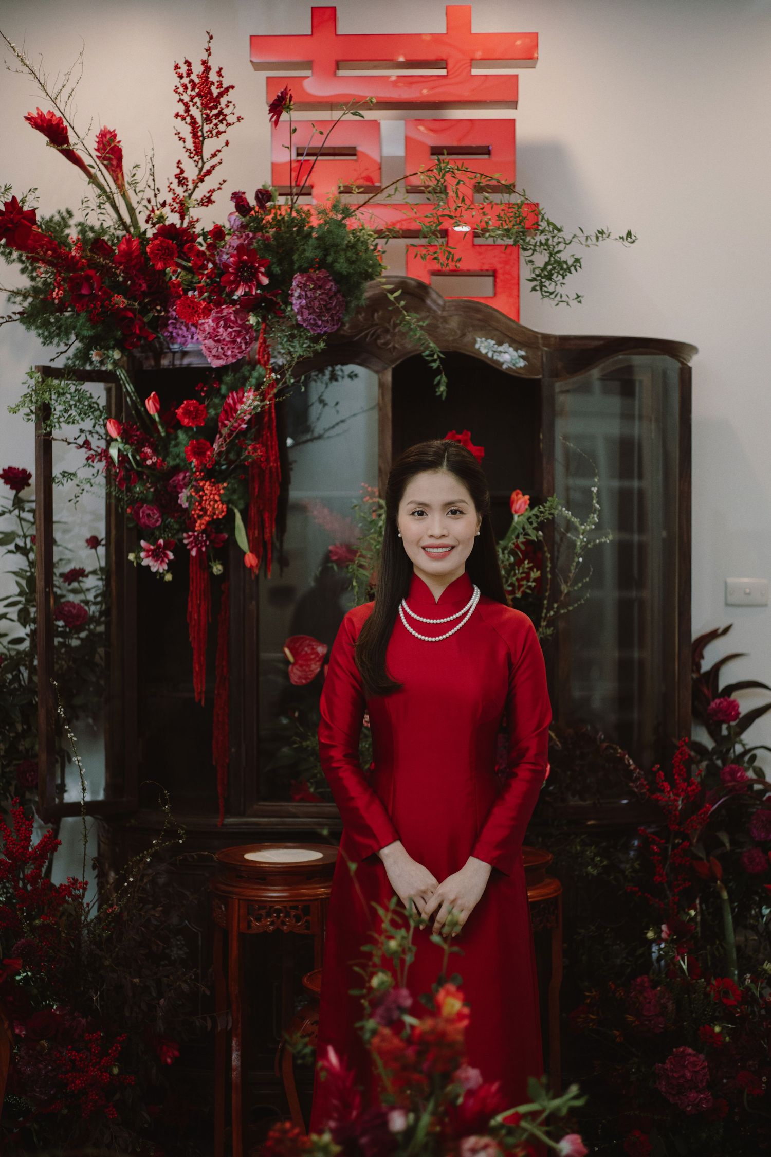 A wedding celebration with traditional Chinese double happiness character decor and red floral arrangements.