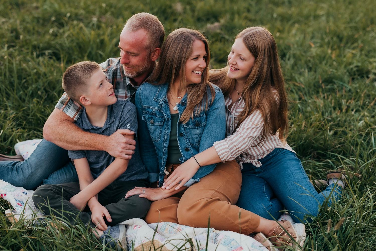 A group sits together on grass in matching denim and brown tones, sharing intimate family moments outdoors.