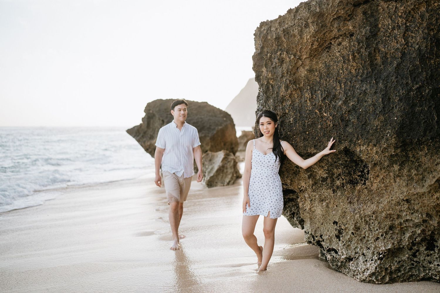 Couple walking together near dramatic coastal rock formations on a sunny beach.