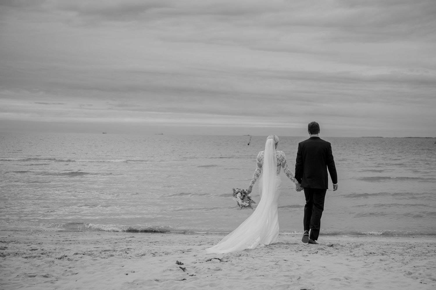 A sequence of black and white beach wedding photos shows a couple walking together along the shoreline.
