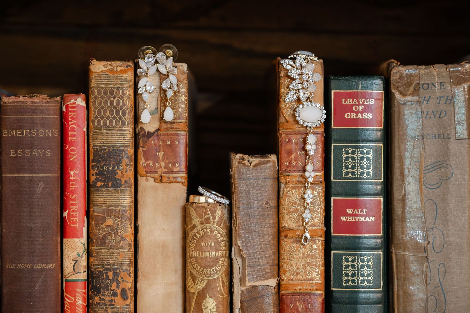 White sleeveless wedding dress hangs elegantly in front of wooden bookshelves filled with books in a library setting.